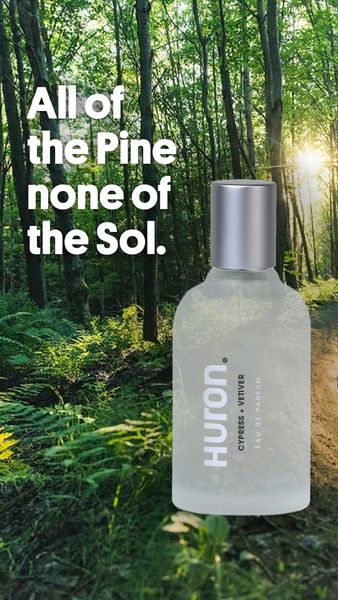 The ad showcases a perfume bottle set against a backdrop of a lush forest illuminated by the sunlight. The perfume bottle is transparent, with a light-colored liquid visible inside, and a silver cap. The forest scene is partially visible through the bottle, suggesting a connection to nature. Text reading "All of the Pine none of the Sol" is layered on the image and to the left of the bottle. The ad's layout is clean and minimalist, emphasizing the perfume bottle and the natural setting.