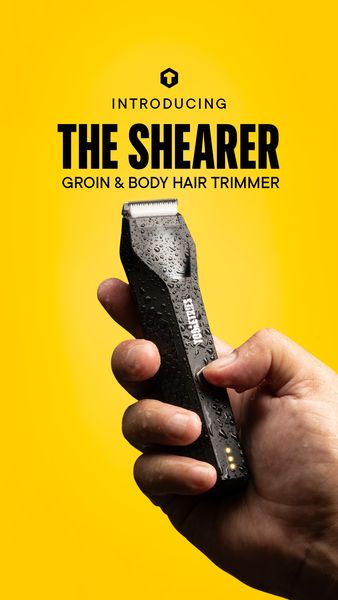 The ad is a vertical shot on a vibrant yellow background. The focus is on a black body hair trimmer held in a right hand with water droplets, set against a gradient background. Text overlay in bold white font reads "INTRODUCING" above "THE SHEARER" in a larger, stylized font, with "GROIN & BODY HAIR TRIMMER" underneath. A logo is present at the top. The trimmer is held by a hand, suggesting its usability. The overall composition is modern and clean, emphasizing the product's sleek design and intended use.