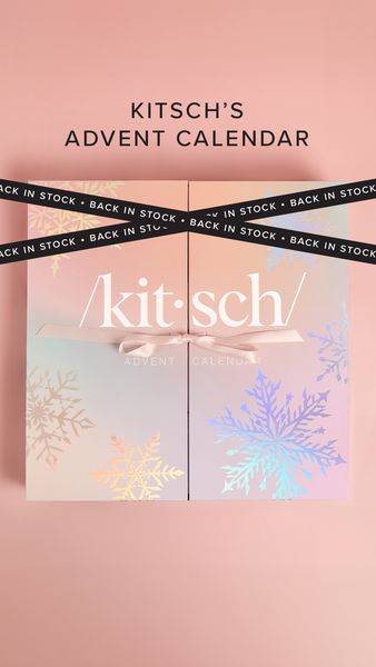 A close-up shot presents a product display, a Christmas-themed Advent calendar. "KITSCH'S ADVENT CALENDAR" is highlighted in the upper section. The calendar features four doors, adorned with snowflake patterns with holographic details. Ribbons marked 'BACK IN STOCK' cross the calendar. The overall aesthetic is festive and appealing, with a soft pink backdrop.