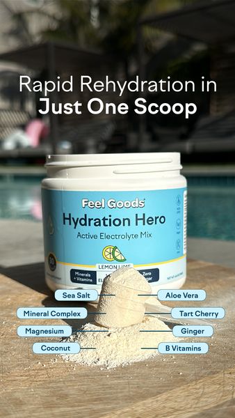An overhead shot showcases a container of hydration mix next to a scoop of the mix on a wooden surface. The banner on the top reads, "Rapid Rehydration in Just One Scoop". The container, prominently positioned, features a light blue label with "Feel Goods Hydration Hero Active Electrolyte Mix Lemon Lime" in large, clear font. Ingredients such as "Sea Salt", "Mineral Complex", "Magnesium", "Coconut", "Aloe Vera", "Tart Cherry", "Ginger", and "B Vitamins" are highlighted around the mix. The background is blurred, suggesting a pool setting.