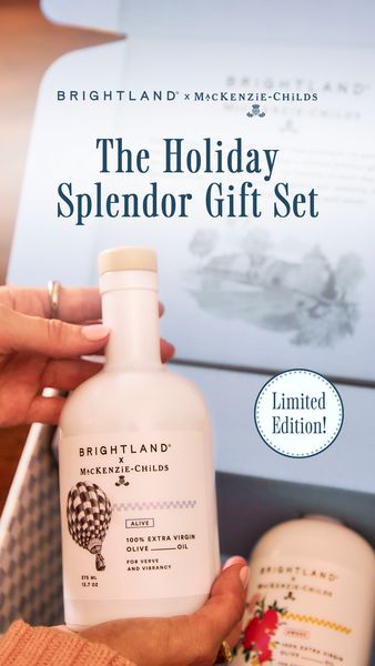 The image showcases a holiday-themed gift set presented in an open box. Soft lighting highlights a white bottle of olive oil held by a person with manicured nails. The bottle labels include the product details and a decorative hot air balloon graphic. A second similar bottle is partially visible. A sticker at the top right corner announces 'Limited Edition!' The background suggests a setting of an elegant holiday gift.