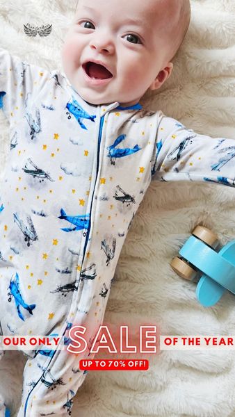 The ad features a close-up shot of a smiling baby lying on a fluffy white blanket. The baby is wearing a light-colored onesie adorned with blue airplanes and yellow stars. A small wooden airplane toy lies by the baby's side. Text overlayed on the bottom of the image reads 'OUR ONLY SALE OF THE YEAR' and 'UP TO 70% OFF!' in bold red letters.