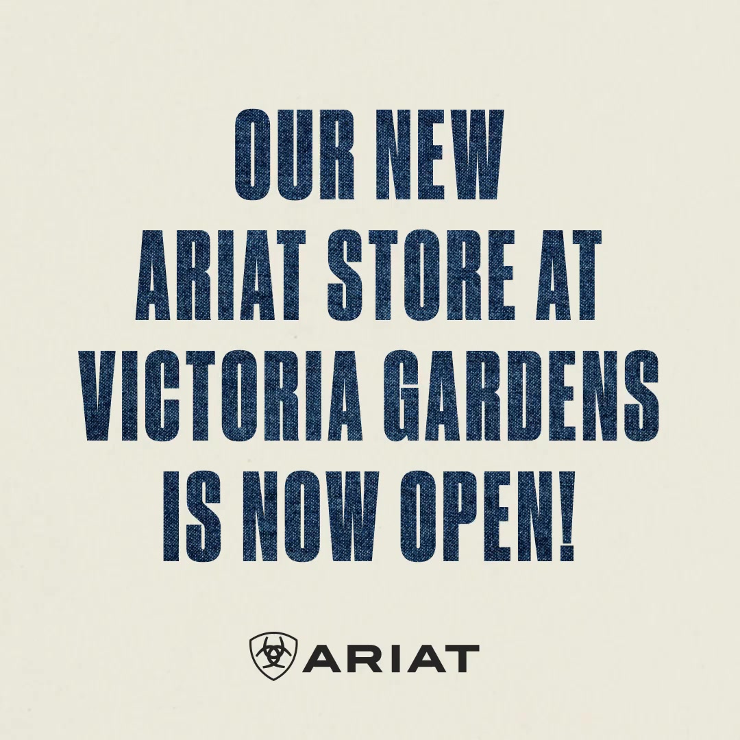 The creative is a text-only graphic with a cream-colored background. Large, dark blue, denim-textured text dominates the image. The text reads: "OUR NEW ARIAT STORE AT VICTORIA GARDENS IS NOW OPEN!". Below the main text, the Ariat logo is displayed. The overall impression is an announcement of a new store opening.