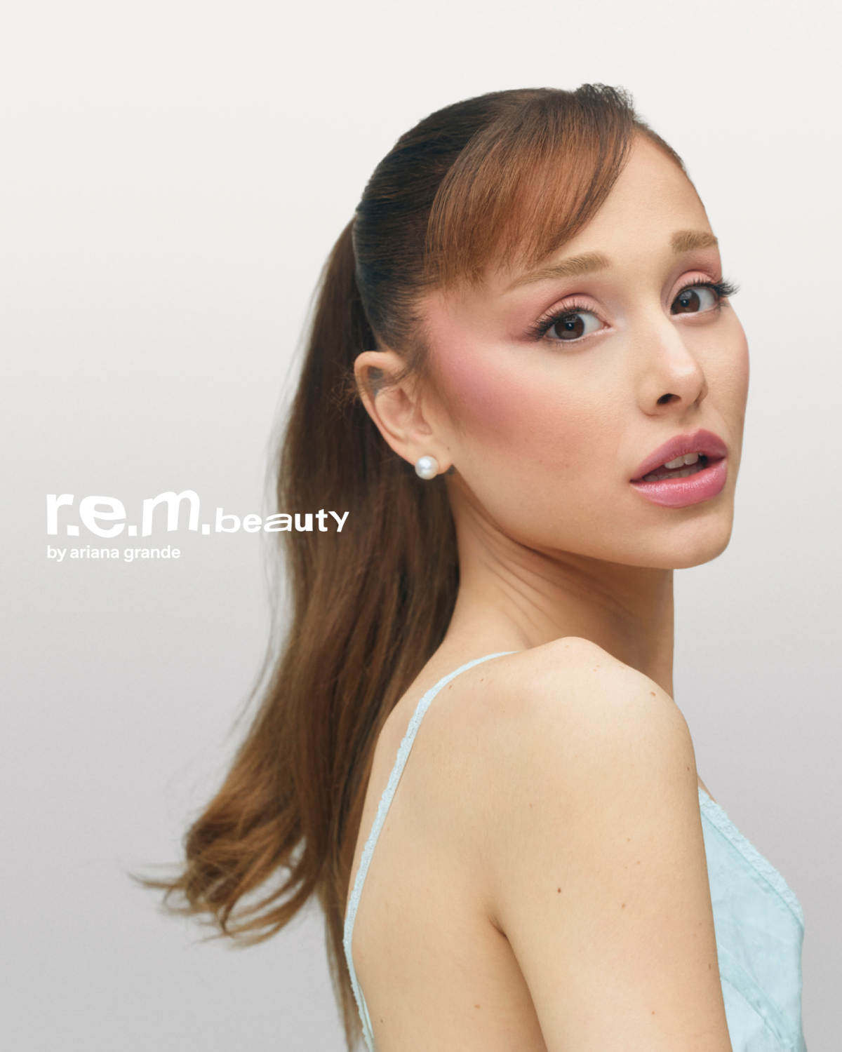 The creative features a close-up shot of Ariana Grande, the founder of R.E.M. Beauty, looking over her shoulder towards the camera. She is wearing subtle makeup and a light blue garment. The R.E.M. Beauty logo and the tagline "by ariana grande" are displayed on the left side of the image. The text "produkte, die deine geschichte erzählen. multifunktionale, mit hautpflege angereicherte hybride und hypersensorische formeln, die kreativität und leichtigkeit miteinander verbinden. exklusiv bei sephora." is overlaid on the image, highlighting the brand's philosophy and product features.