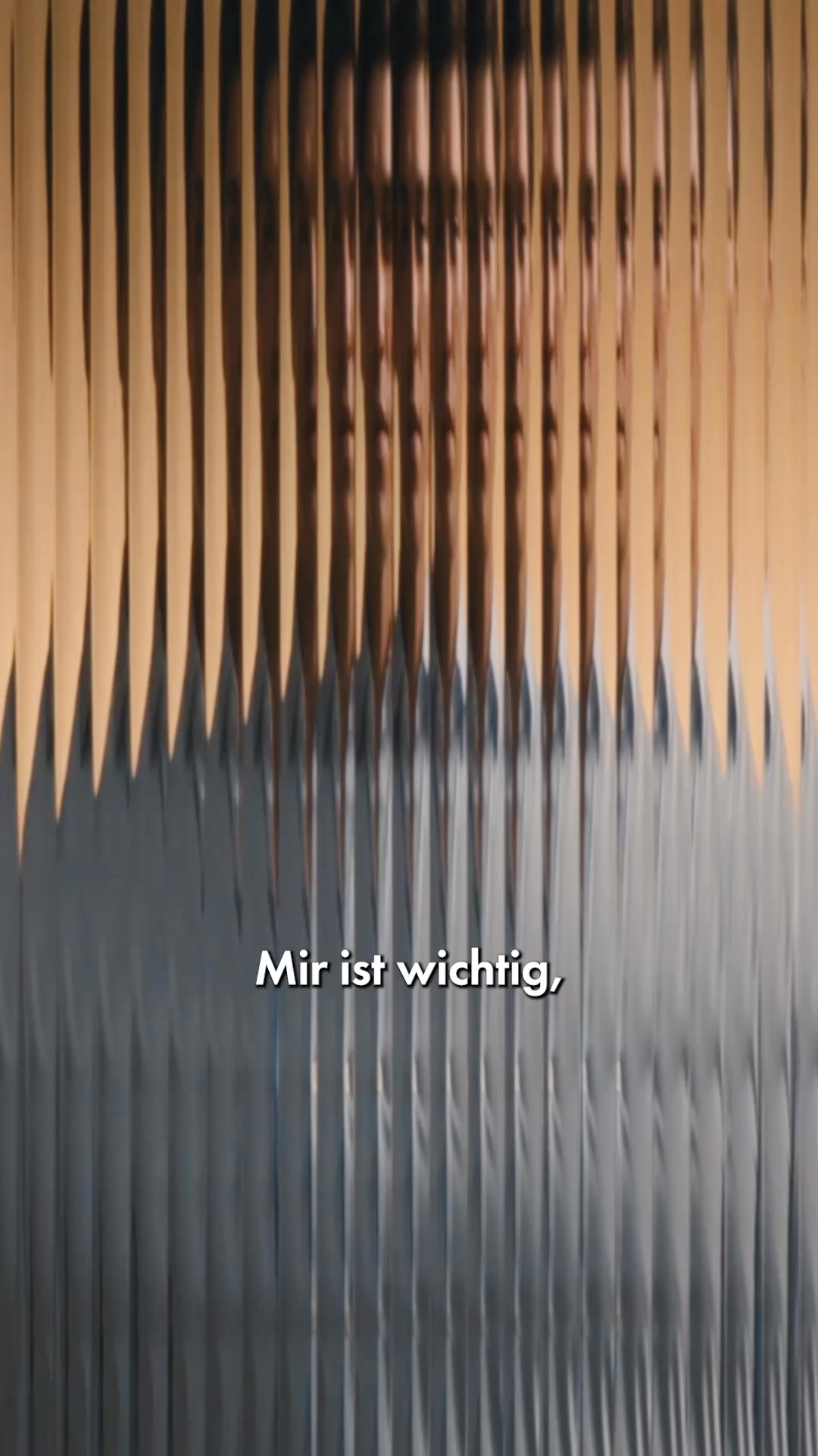 The creative features a textured glass effect with vertical lines, creating a distorted view of a person's face in the upper portion. The lower portion is a solid grey. White text overlaid on the grey section reads "Mir ist wichtig," which translates to "It is important to me." The overall aesthetic is abstract and visually intriguing, with the text serving as the primary message.