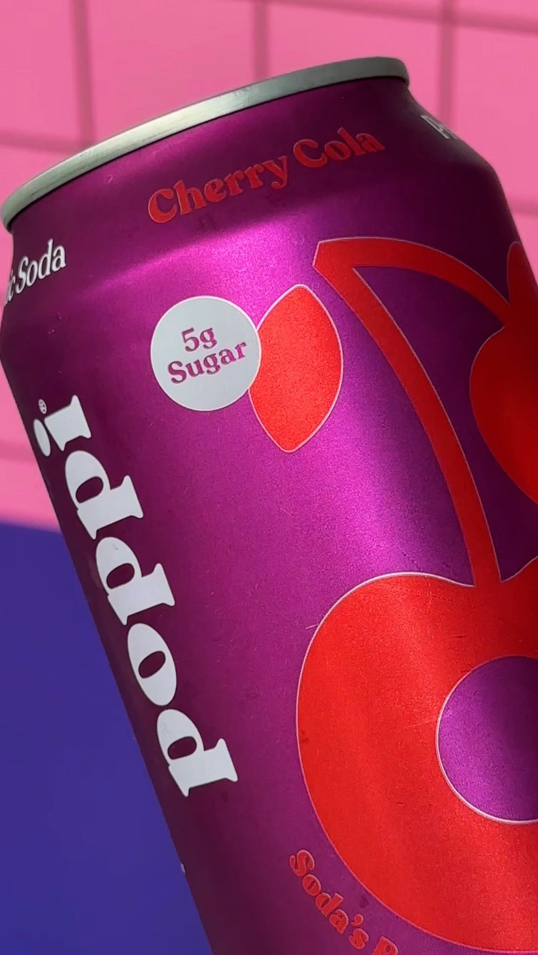 A close-up shot of a Poppi Cherry Cola can with a vibrant pink and blue background. The can is metallic purple with red lettering and a large cherry graphic. A small white circle on the can highlights "5g Sugar". The text "like this post to claim the weekend vibe 😌🥤" is overlaid on the image, encouraging engagement.