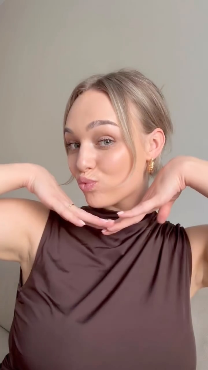 A woman with blonde hair pulled back is puckering her lips and holding her hands to her face. She is wearing a brown sleeveless top. The background is a plain, light-colored wall. The text overlay reads "Never going back to other foundations 🤍 @merodacosmetics". The ad copy mentions the product is a lightweight, smooth, and breathable foundation that blends perfectly into the skin tone, and also highlights a soft brush. A discount code 'DEMI20' for 20% off is provided.