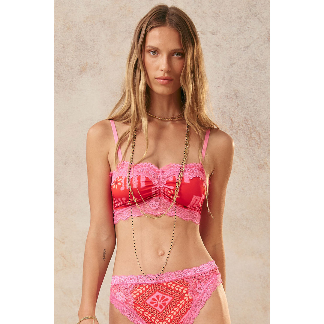 A woman with long blonde hair stands against a textured, neutral background. She is wearing a red and pink patterned bralette with pink lace trim and matching pink lace-trimmed underwear. She is adorned with multiple gold necklaces. The text "There's a version of you that wears things like this. She's not far away. New arrivals online now." is overlaid on the image.