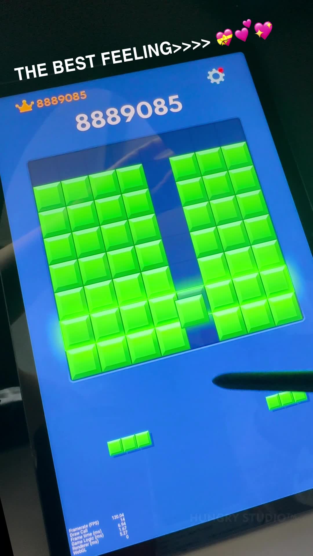 A screen recording shows a mobile game called Block Blast. The game screen is bright blue with many green blocks arranged in columns. The score "8889085" is displayed prominently at the top of the screen, along with a crown icon. Text overlayed at the top reads "THE BEST FEELING>>>>" accompanied by heart emojis. The bottom left of the screen shows game performance statistics. The overall impression is of a highly satisfying and successful gameplay moment.