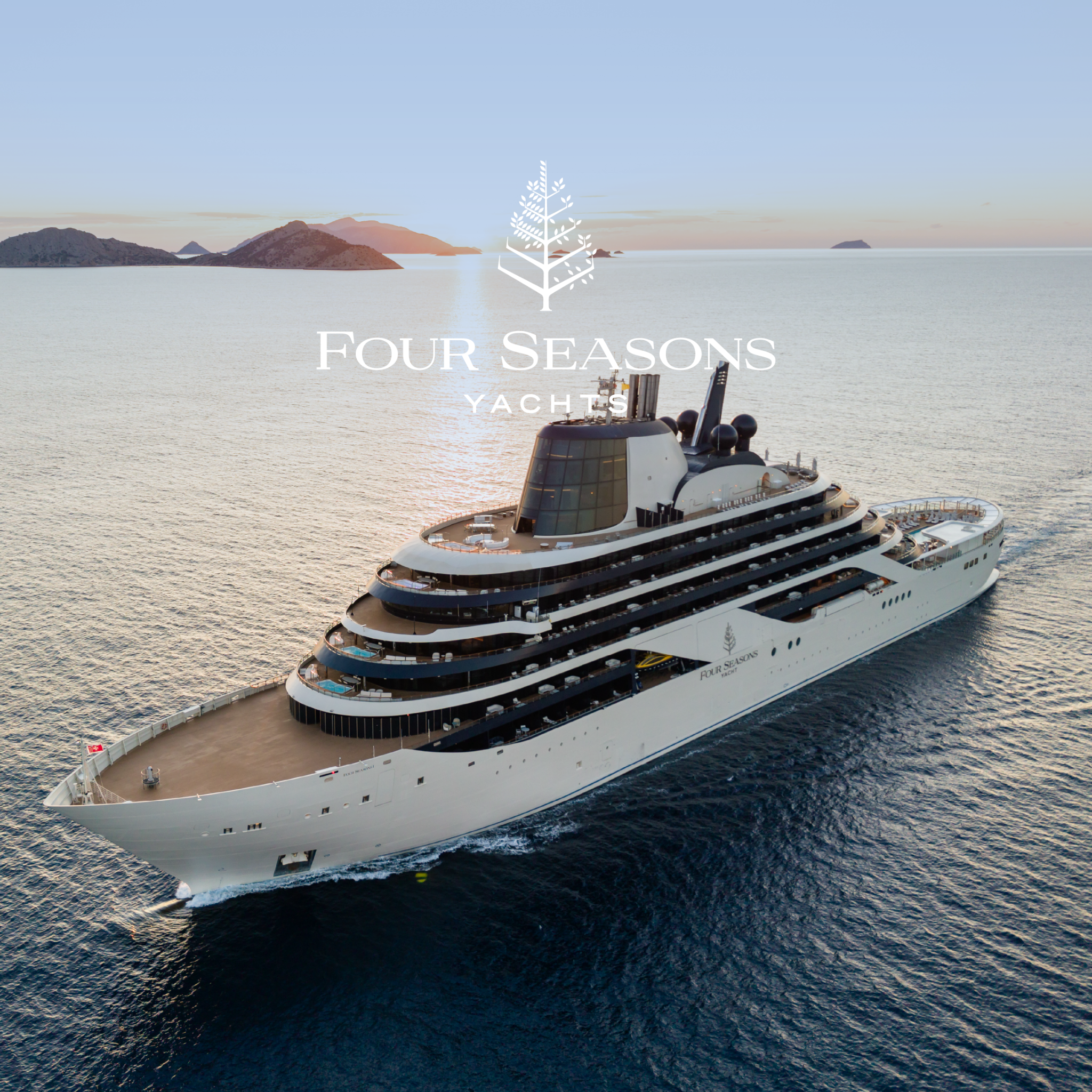 An aerial shot shows a luxurious Four Seasons yacht sailing on calm, blue water during sunset. The sky is a soft gradient of blue and orange, with distant islands visible on the horizon. The yacht's elegant design is highlighted, featuring multiple decks with lounge areas and pools. White text overlaying the image reads "Festive travel reimagined." The Four Seasons Yachts logo is also visible on the yacht and subtly in the upper center of the image.