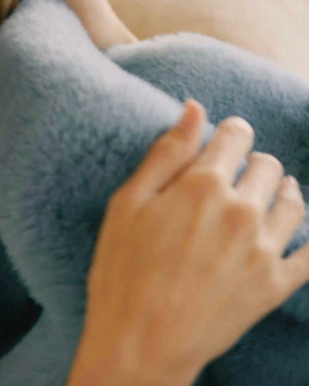A close-up shot shows a person's hands gently touching a soft, light blue, fuzzy material. The lighting is warm and soft, suggesting a cozy indoor setting. The text overlay reads "Feels like fall," evoking a sense of comfort and the changing seasons.