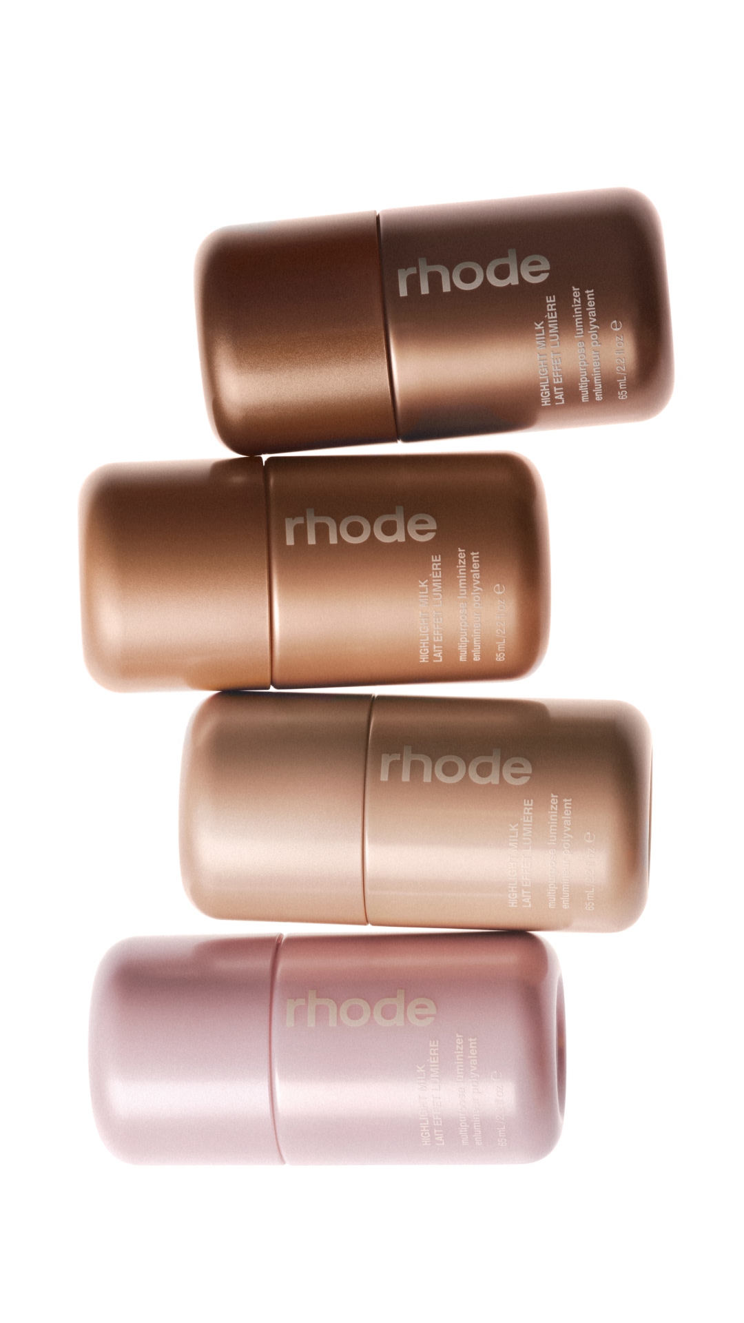 A clean, studio shot features four Rhode Highlight Milk bottles stacked vertically against a white background. The bottles are metallic and come in shades of bronze, rose gold, and pink. The text "rhode" is prominently displayed on each bottle. Below the brand name, smaller text reads "HIGHLIGHT MILK" and "LAIT EFFET LUMIÈRE," along with "multipurpose luminizer" and "enluminateur polyvalent." The hook "meet highlight milk 🌟" is overlaid on the image.