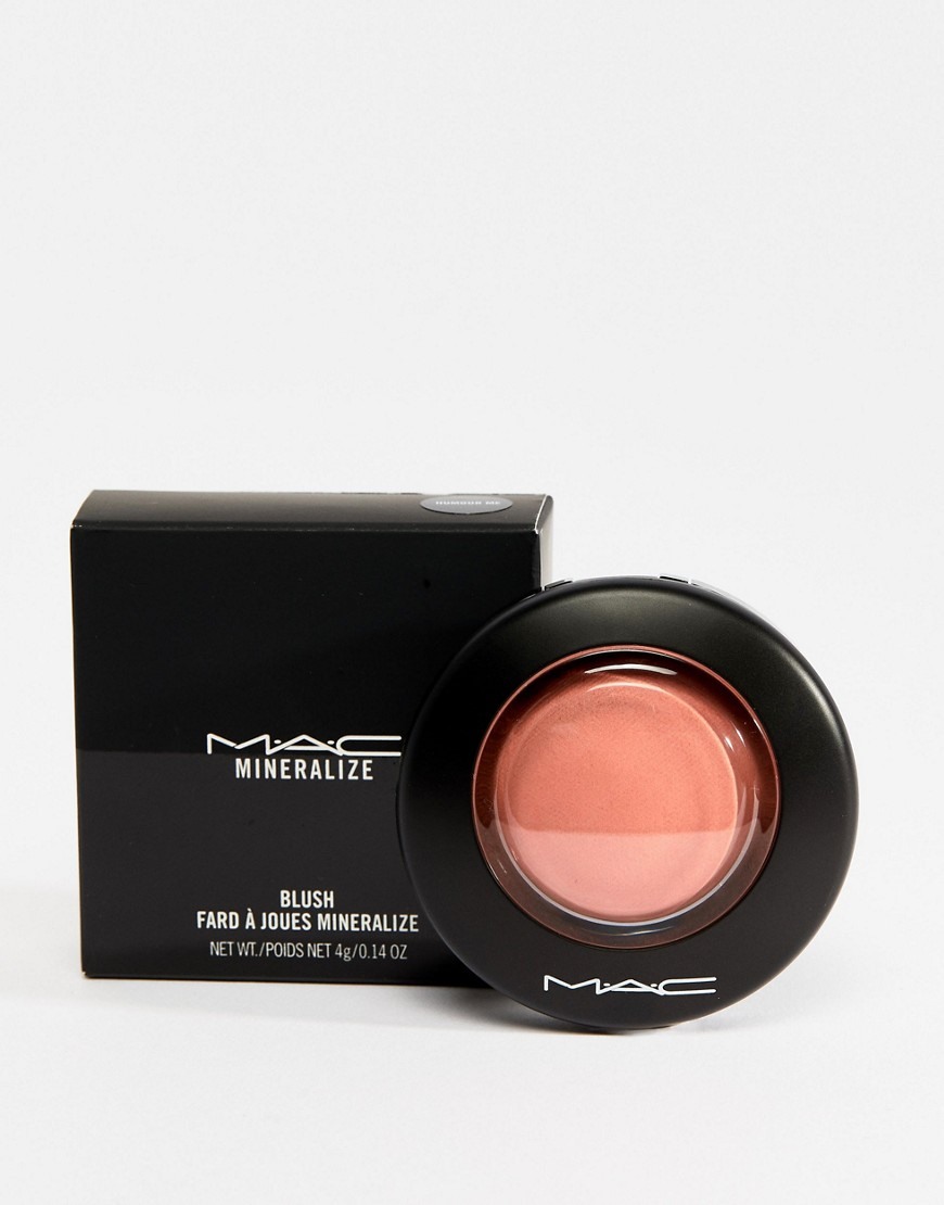 A black box and a round, black compact of MAC blush are shown against a white background. The blush compact is open, revealing a peachy-pink powder with a subtle sheen. Text on the box reads "MAC MINERALIZE BLUSH FARD À JOUES MINERALIZE NET WT./POIDS NET 4g/0.14 OZ". The hook text, "Vous venez d'arriver sur ASOS ? Chez nous, il y en a pour tous les styles et pour tous les goûts. Plus de 850 marques vous attendent là, tout de suite, maintenant ✨", is overlaid on the image.