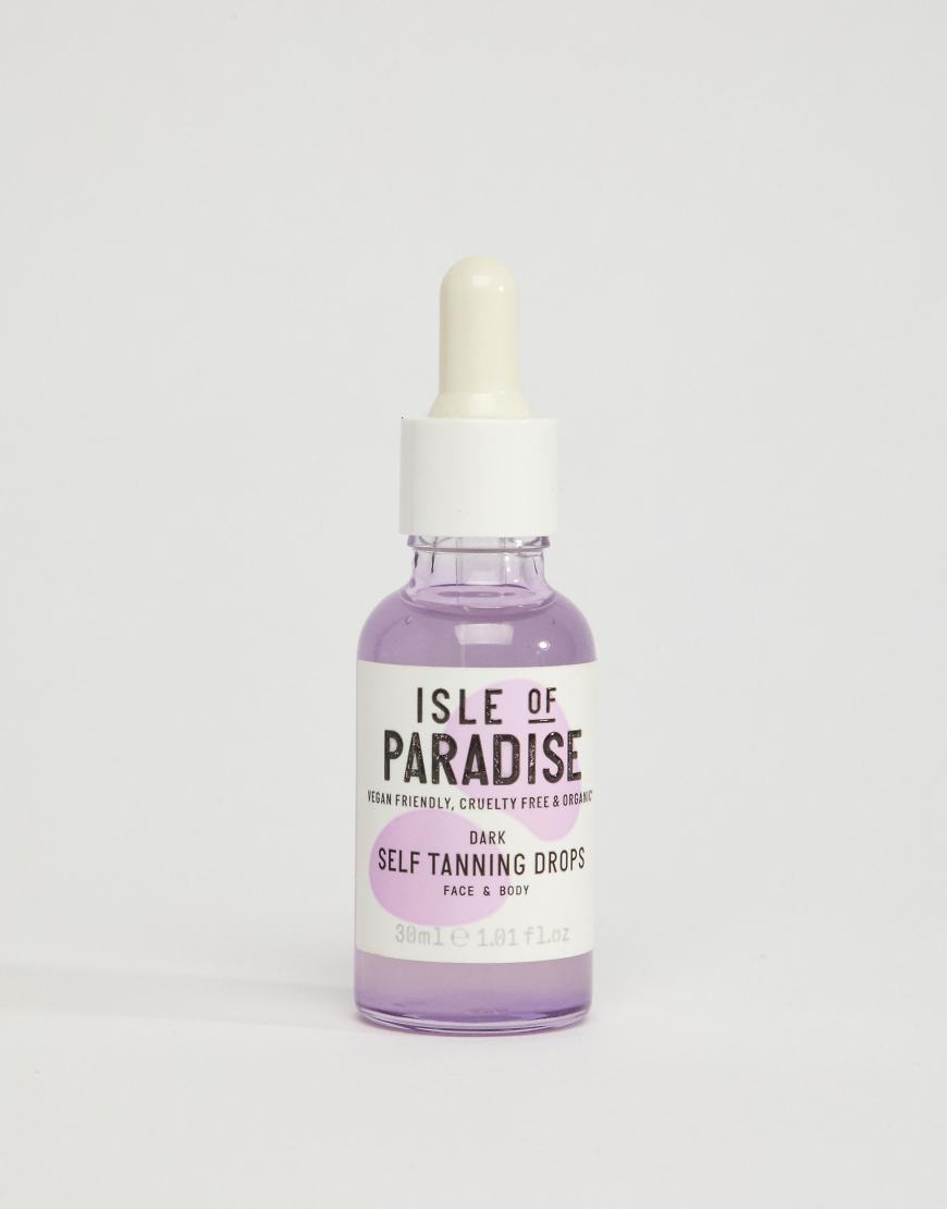 A product shot of Isle of Paradise Self Tanning Drops in Dark. The bottle is purple with a white dropper lid. Text on the bottle reads "ISLE OF PARADISE" in large black letters, with smaller text below that says "VEGAN FRIENDLY, CRUELTY FREE & ORGANIC". Below that, in a pink circle, it says "DARK SELF TANNING DROPS". The bottom of the bottle has "30ml e 1.01 Fl.Oz" written on it. The background is plain white. The hook text "¿Todas tus marcas favoritas en un solo lugar?" is overlaid on the image.