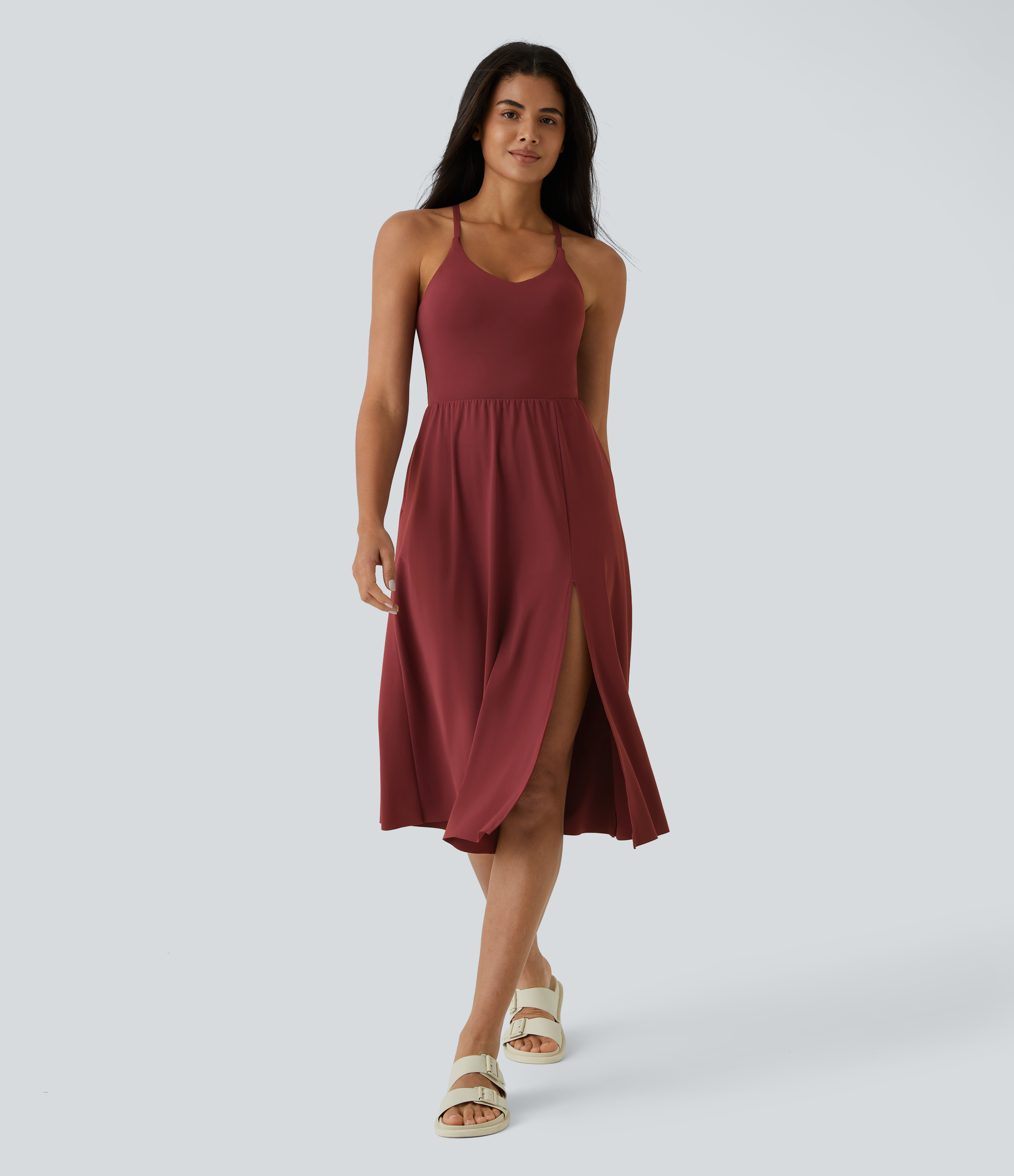 A woman walks towards the camera wearing a maroon, sleeveless midi dress with a high slit on the left side. She is also wearing cream-colored sandals. The background is a plain light gray. Text overlays on the image read: "Perfect for Fashion and Function!", "Great for indoor and outdoor activities!", and "Get yours NOW!" The overall tone is aspirational, showcasing a stylish and versatile outfit.