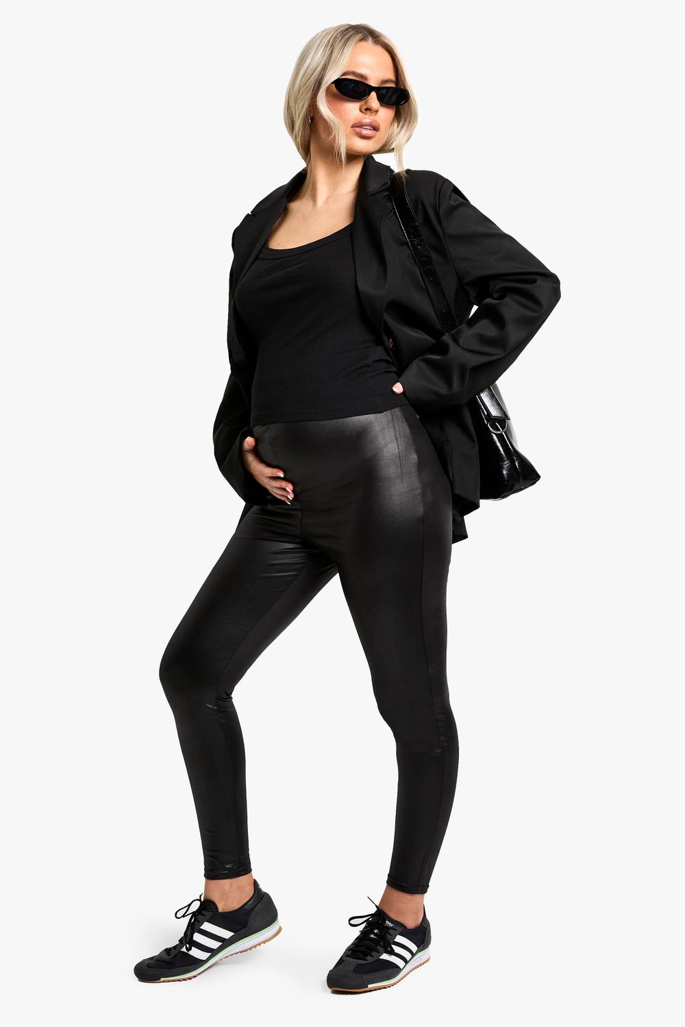 A pregnant model stands with one hand on her belly, wearing a black blazer over a black tank top and black faux leather leggings. She is also wearing black sneakers and sunglasses. The background is a plain white. On-screen text reads "Cyber deals are now LIVE 🚨 Shop 35% off EVERYTHING* for a limited time only ✨ Plus, shop an extra 10% off with code SOCIAL10 ✨Order before midnight for next day delivery 💌".