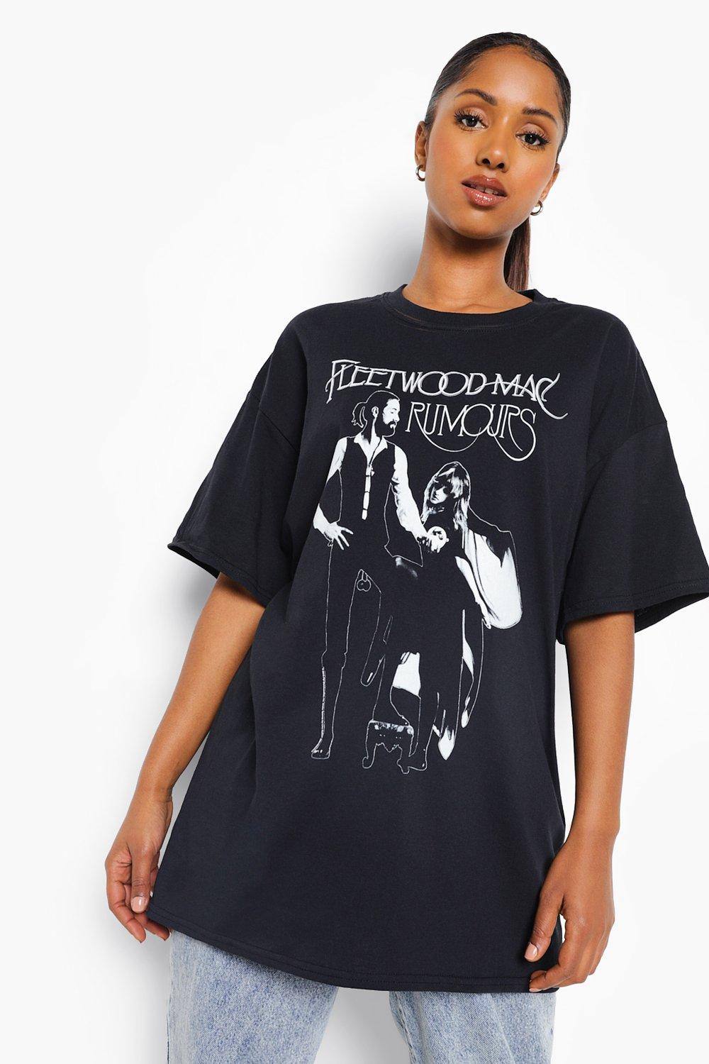 A woman is shown from the chest up, wearing a black t-shirt with a graphic print of the band Fleetwood Mac and the album title 'Rumours'. The t-shirt has a loose, oversized fit. The background is plain white. The text '50% korting op alles!' is overlaid on the image in a large, bold font, with a red siren emoji preceding it and a red heart-eyes emoji following it.