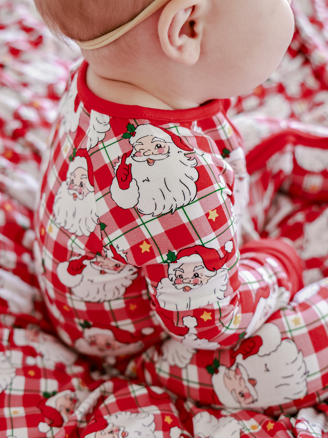 A close-up shot of a baby wearing red and white plaid pajamas with a Santa Claus print. The baby is lying down, and the focus is on the pajamas and the baby's back and shoulder. The text overlay reads "🍪HO-HO-HURRY!! Our best prints go FAST!" The overall impression is festive and hints at a limited-time sale on holiday-themed baby clothing.