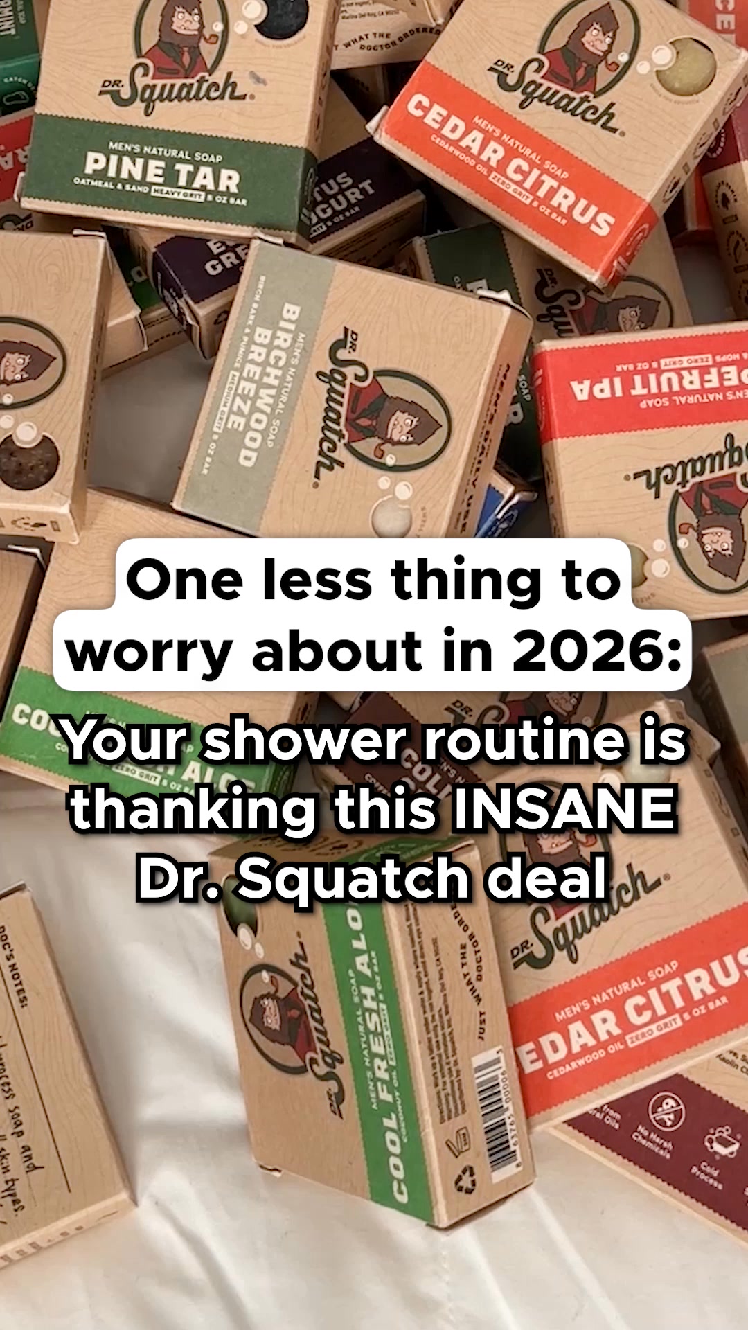 A pile of Dr. Squatch soap bars is shown. White text overlaid on the image reads "One less thing to worry about in 2026: Your shower routine is thanking this INSANE Dr. Squatch deal". The soaps are packaged in brown cardboard boxes with the Dr. Squatch logo and product names like "Pine Tar", "Cedar Citrus", and "Birchwood Breeze" visible.