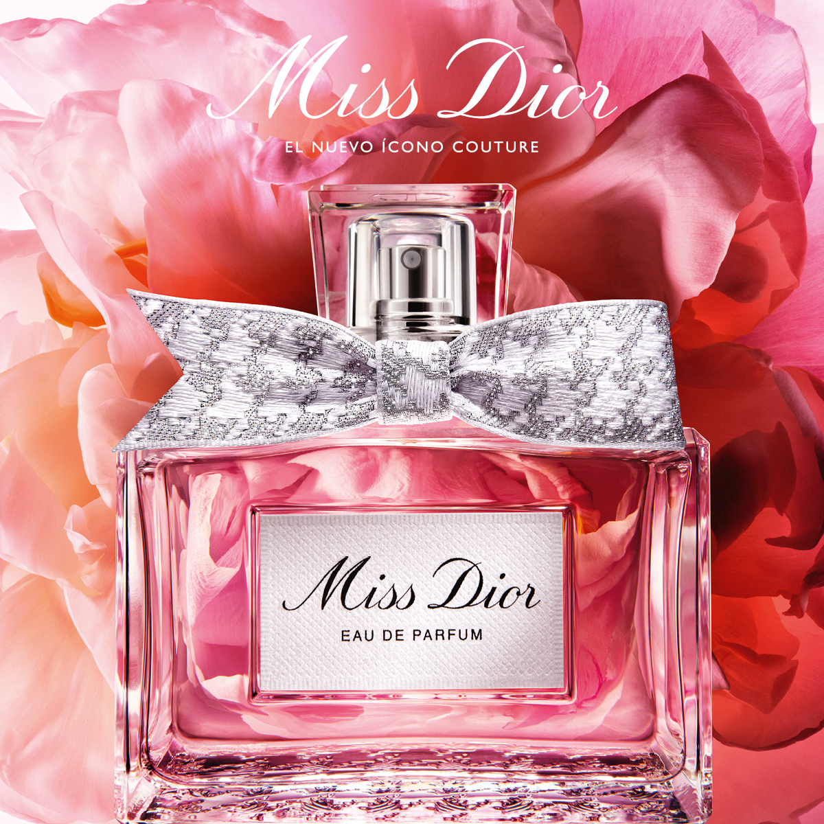 A close-up, studio shot of a Miss Dior Eau de Parfum bottle is presented against a soft-focus background of large, pink and red flower petals. The bottle features a prominent silver bow with a lace-like pattern around its neck. White text overlays the image, with the main headline in a script font reading "Miss Dior" and a smaller line below it stating "EL NUEVO ÍCONO COUTURE". The bottle's label also reads "Miss Dior" and "EAU DE PARFUM".