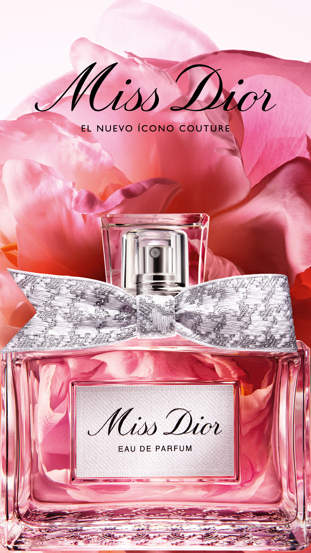A close-up, eye-level shot of a Miss Dior Eau de Parfum bottle is presented against a soft, blurred background of large pink flower petals. The bottle is clear glass, revealing the pink fragrance inside, and is adorned with a delicate, silver-patterned bow around its neck. The brand name "Miss Dior" is prominently displayed in elegant script at the top of the image, followed by the Spanish text "EL NUEVO ÍCONO COUTURE" (The New Couture Icon). Below the brand name on the bottle's label, it reads "Miss Dior EAU DE PARFUM".