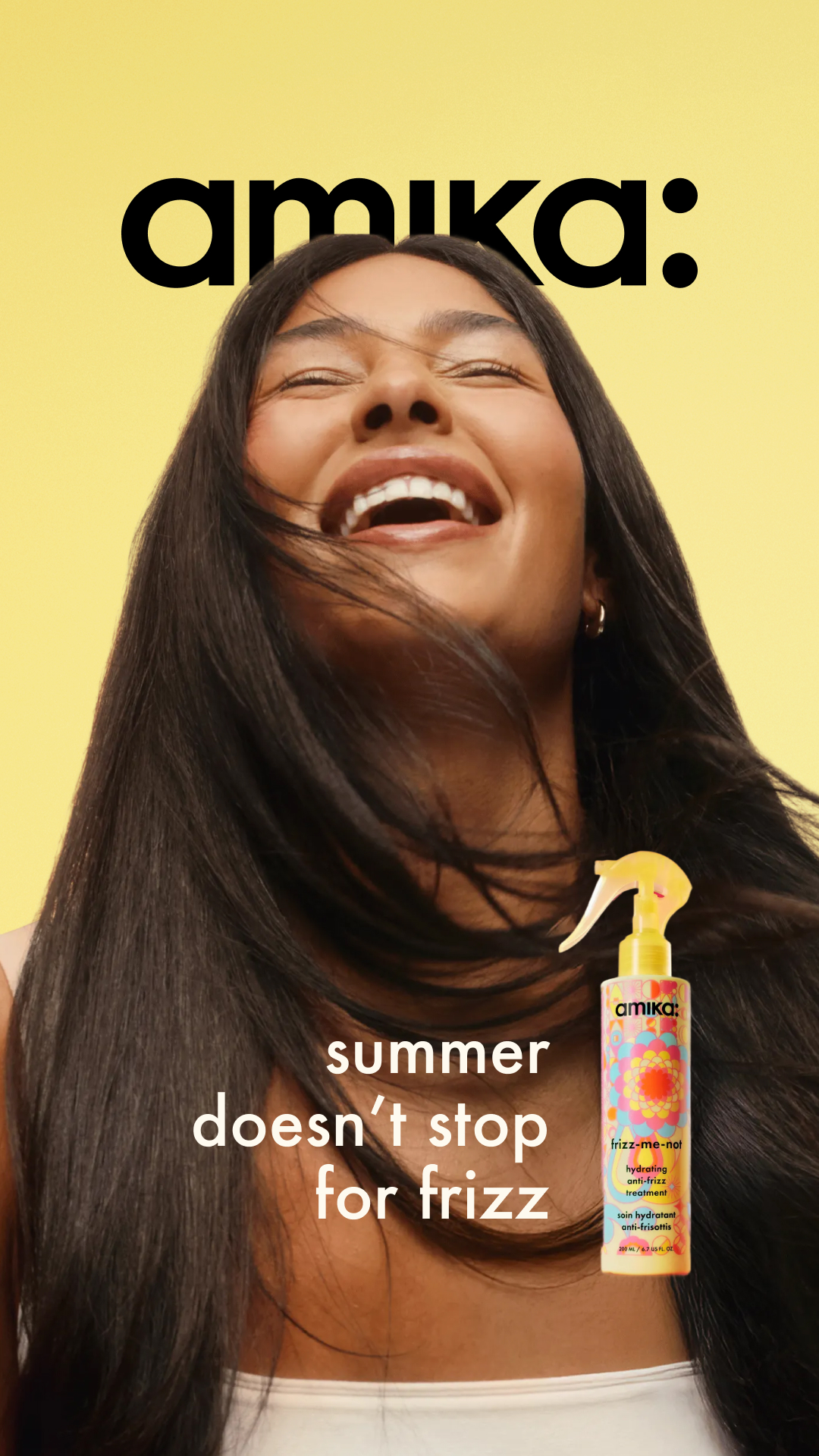 A woman with her eyes closed and mouth open in laughter is shown against a bright yellow background. Her hair is flowing, and she is holding a bottle of Amika frizz-me-not product. White text overlayed on the image reads "summer doesn't stop for frizz." The overall impression is one of carefree joy and freedom from hair concerns during the summer season.