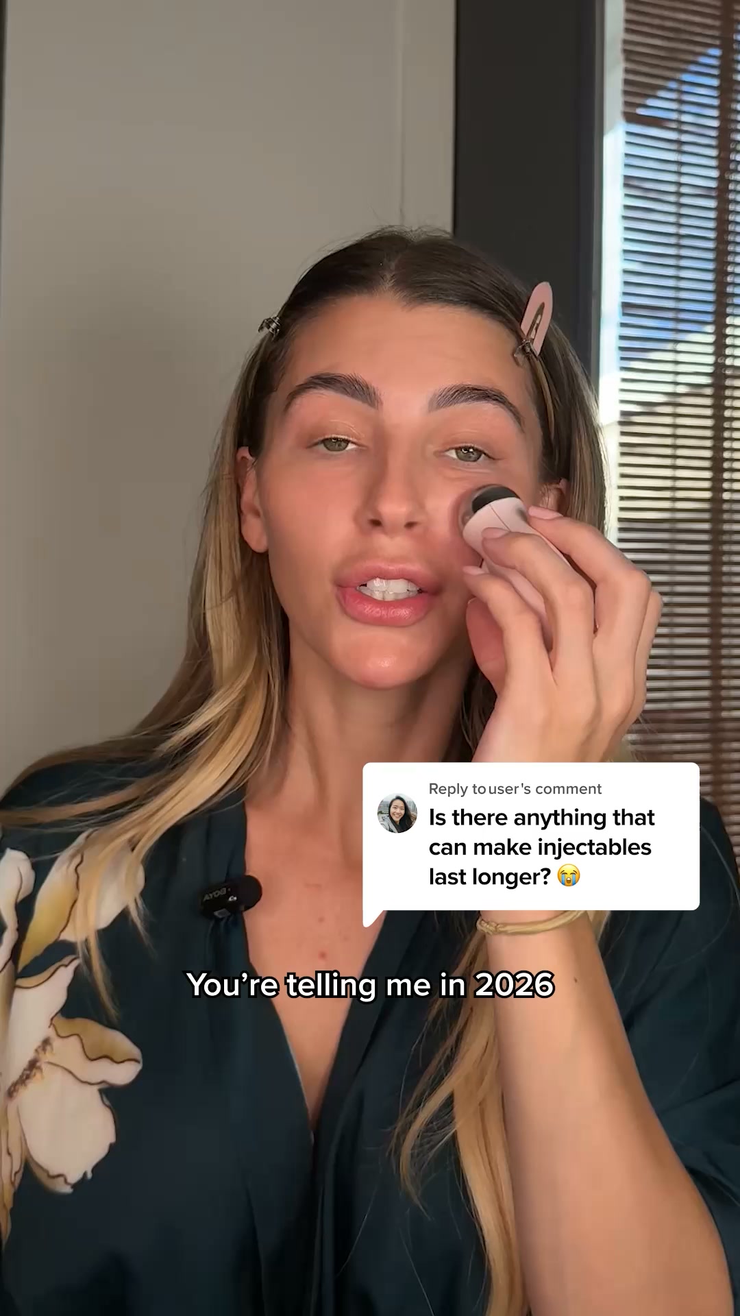 A woman is shown applying a NuFace device to her cheek while looking at the camera. A comment box is overlaid on the right side of the screen, displaying a question from a user about making injectables last longer, accompanied by a crying emoji. Below the woman's chin, text reads "You're telling me in 2026". The overall impression is a response to a viewer's question about cosmetic procedures and longevity, with the product being presented as a potential solution.