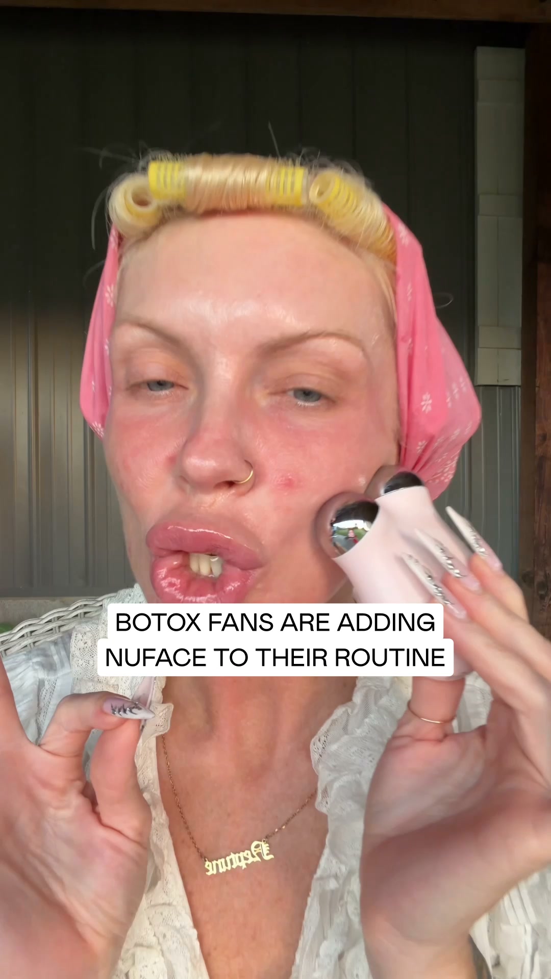 A close-up shot of a woman with blonde hair in curlers and a pink headscarf is using a NuFace device on her cheek. She is wearing a white lace top and a gold necklace. White text overlaid on the image reads "BOTAX FANS ARE ADDING NUFACE TO THEIR ROUTINE". The woman has full lips and is looking towards the camera. The background is blurred and appears to be outdoors.