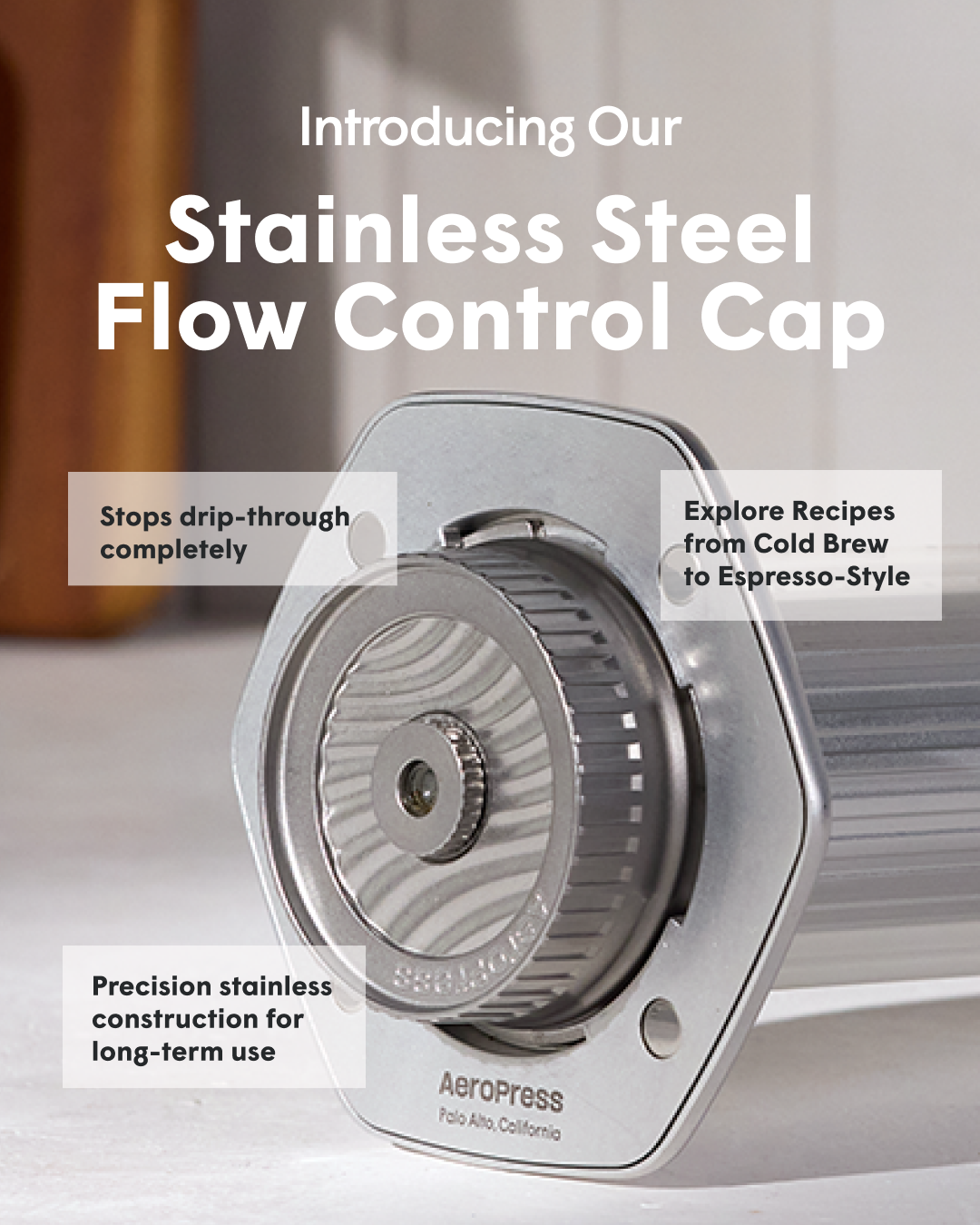 A close-up, angled shot of the AeroPress Stainless Steel Flow Control Cap is shown. Text overlays highlight key features: 'Stops drip-through completely', 'Precision stainless construction for long-term use', and 'Explore Recipes from Cold Brew to Espresso-Style'. The AeroPress logo and location are visible on the product itself.