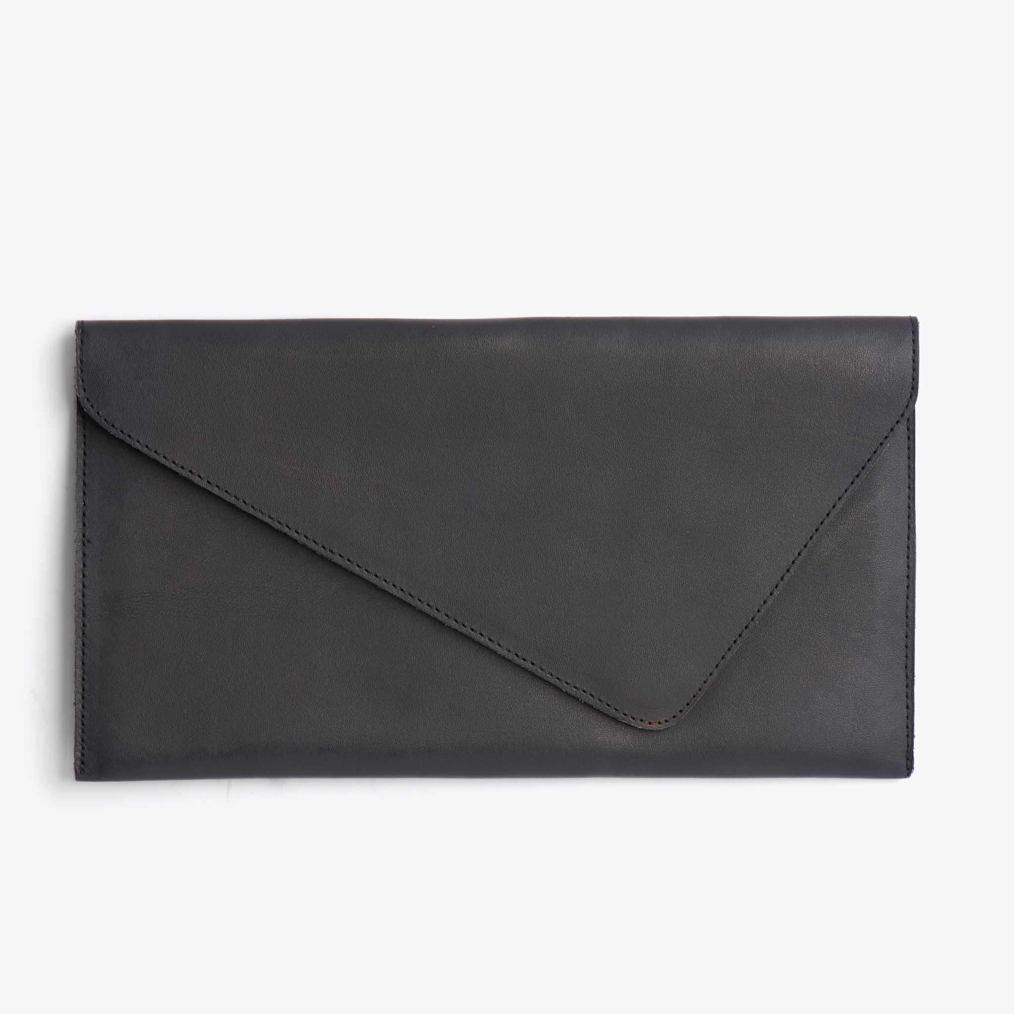 A black leather clutch is shown against a plain white background. The clutch has a flap closure with a diagonal seam. The text "Make styling effortless with shoes you can wear all season long. 🌱" is overlaid on the image. The creative focuses on the product itself, presented in a clean, studio-like setting.