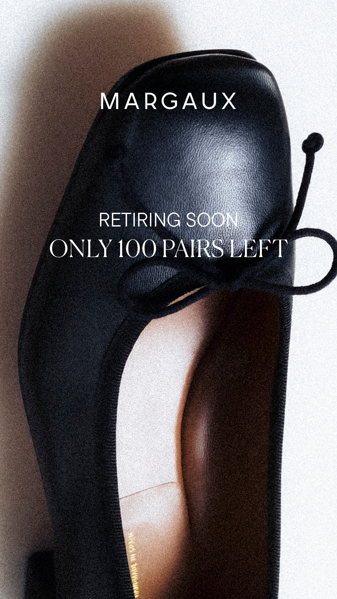 A close-up, slightly grainy, overhead shot of a black leather ballet flat shoe. The brand name "MARGAUX" is displayed in large white capital letters at the top of the image. Below the brand name, in white text, it reads "RETIRING SOON" and "ONLY 100 PAIRS LEFT". The shoe is the primary focus, with its delicate bow and stitching visible. The background is a soft, out-of-focus gradient of light and shadow.