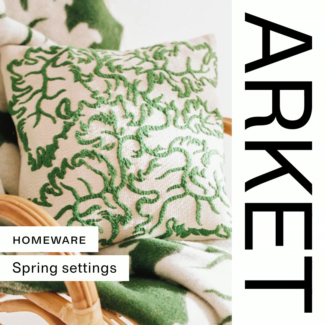 A close-up shot focuses on a cream-colored throw pillow with an intricate green embroidered vine pattern. The pillow rests on a wicker chair, partially covered by a green and white striped blanket. To the left of the pillow, two white text boxes are overlaid on the image. The top box reads "HOMEWARE" in black text, and the bottom box reads "Spring settings" in black text. The right side of the image features the word "ARKET" in large, black, sans-serif capital letters, oriented vertically.