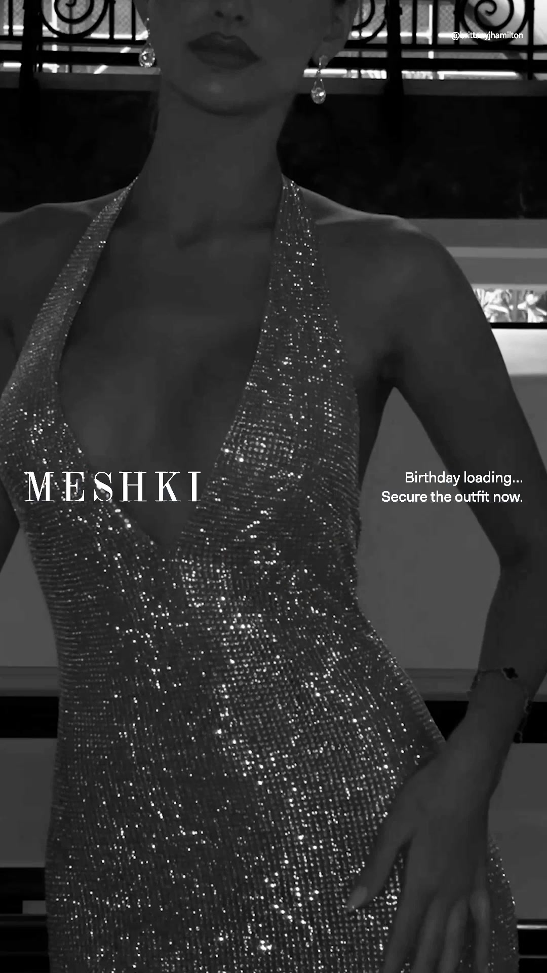 A black and white, close-up shot of a woman wearing a sparkly, halter-neck dress. The text "MESH KI" is overlaid on the left side of the dress. On the right side, the text "Birthday loading... Secure the outfit now." is displayed. The overall aesthetic is glamorous and celebratory, hinting at an upcoming special occasion.