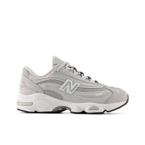A clean, studio shot of a single New Balance sneaker in a light grey colorway against a white background. The shoe is positioned in profile, showcasing its design details. Overlayed on the shoe is the Italian text "Una gamma di prodotti diversificata, adatta a ogni lifestyle," which translates to "A diverse range of products, suitable for every lifestyle." The text is placed centrally on the shoe's side panel.
