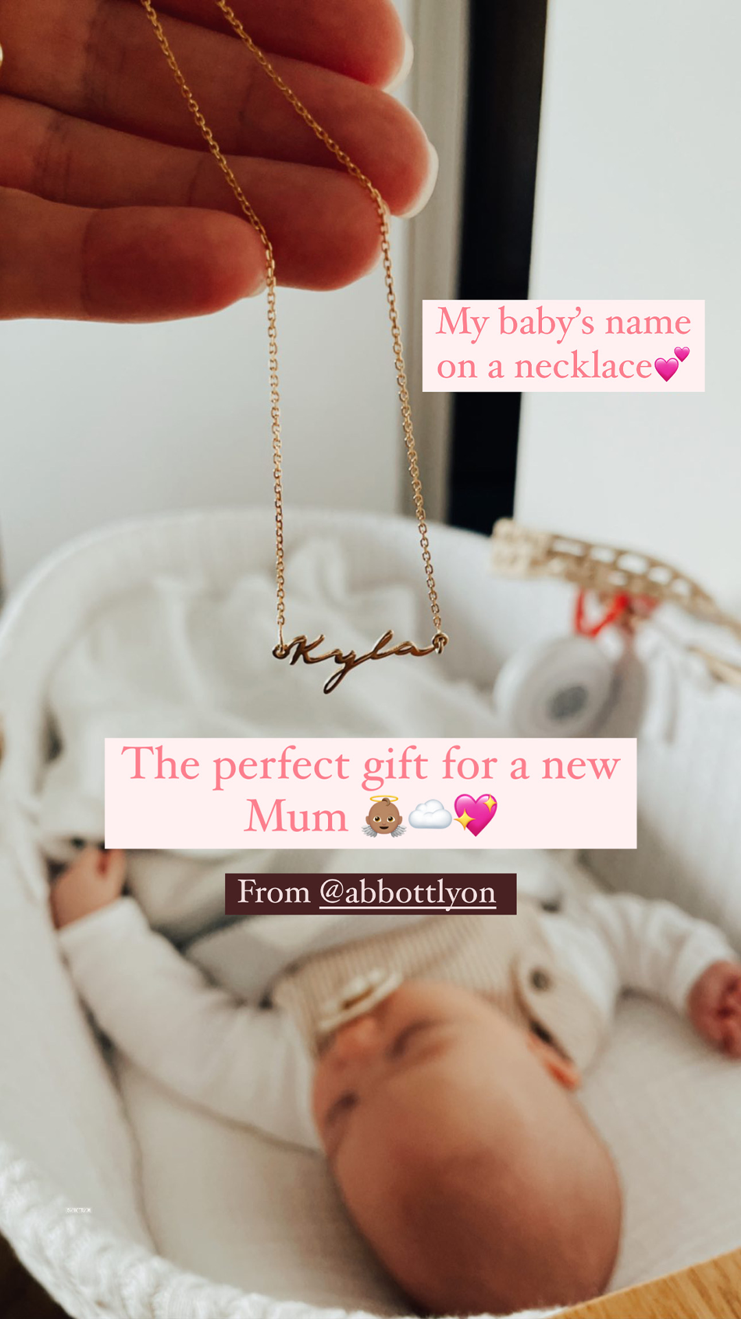 A close-up shot shows a hand holding a delicate gold necklace with the name "Kyla" scripted on it. In the blurred background, a newborn baby sleeps peacefully in a bassinet. Pink text overlays read "My baby's name on a necklace" and "The perfect gift for a new Mum" with accompanying emojis. Below this, a dark brown banner states "From @abbottlyon."