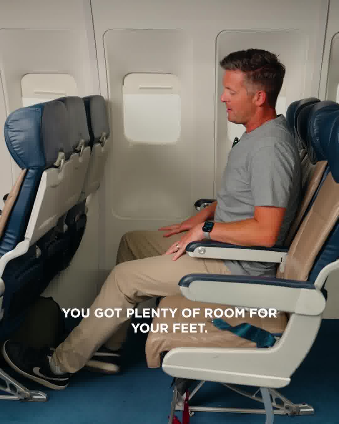 A man is sitting in an airplane seat, looking to his right. The text "YOU GOT PLENTY OF ROOM FOR YOUR FEET." is overlaid on the image, with the words "YOUR FEET" positioned over the man's legs and the seat in front of him. The scene is focused on demonstrating the legroom available in the airplane cabin.