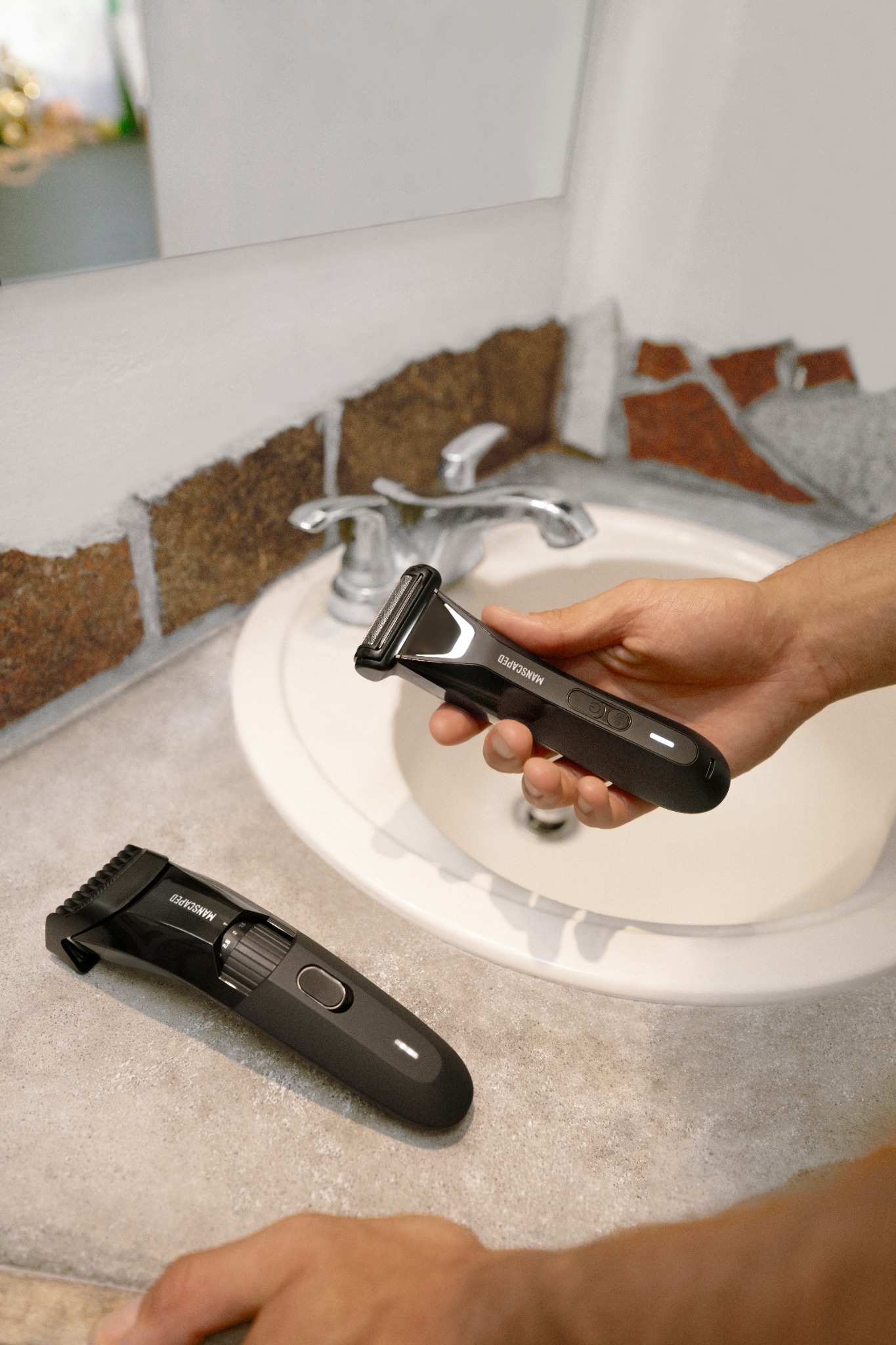 A hand holds a black Manscaped body hair trimmer over a bathroom sink. Another identical trimmer lies on the counter next to the sink. The image has text overlays that highlight the product bundle and its benefits, including "The Lawn Mower® 5.0 Ultra Groin & Body Hair Trimmer" and "The Beard Hedger® Beard Trimmer." The text also mentions "Waterproof for easy clean-up" and "Online Exclusive." The ad promotes a bundle deal with a call to action to "Join over 14 million men worldwide who trust MANSCAPED®!"