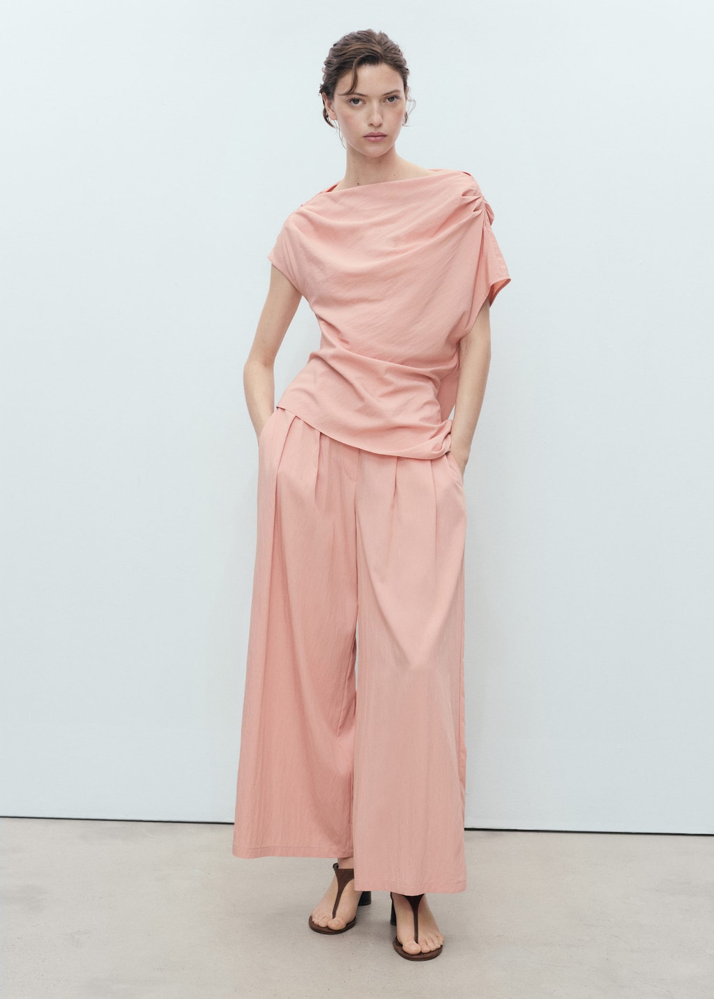 A woman stands against a white background wearing a pastel pink off-the-shoulder top and wide-leg pants. She has her hands in her pockets and is looking at the camera. The text overlay asks, "What will you wear this spring?" The ad copy encourages viewers to refresh their wardrobes with light clothing in pastel colors and eye-catching patterns from Mango's new collection.