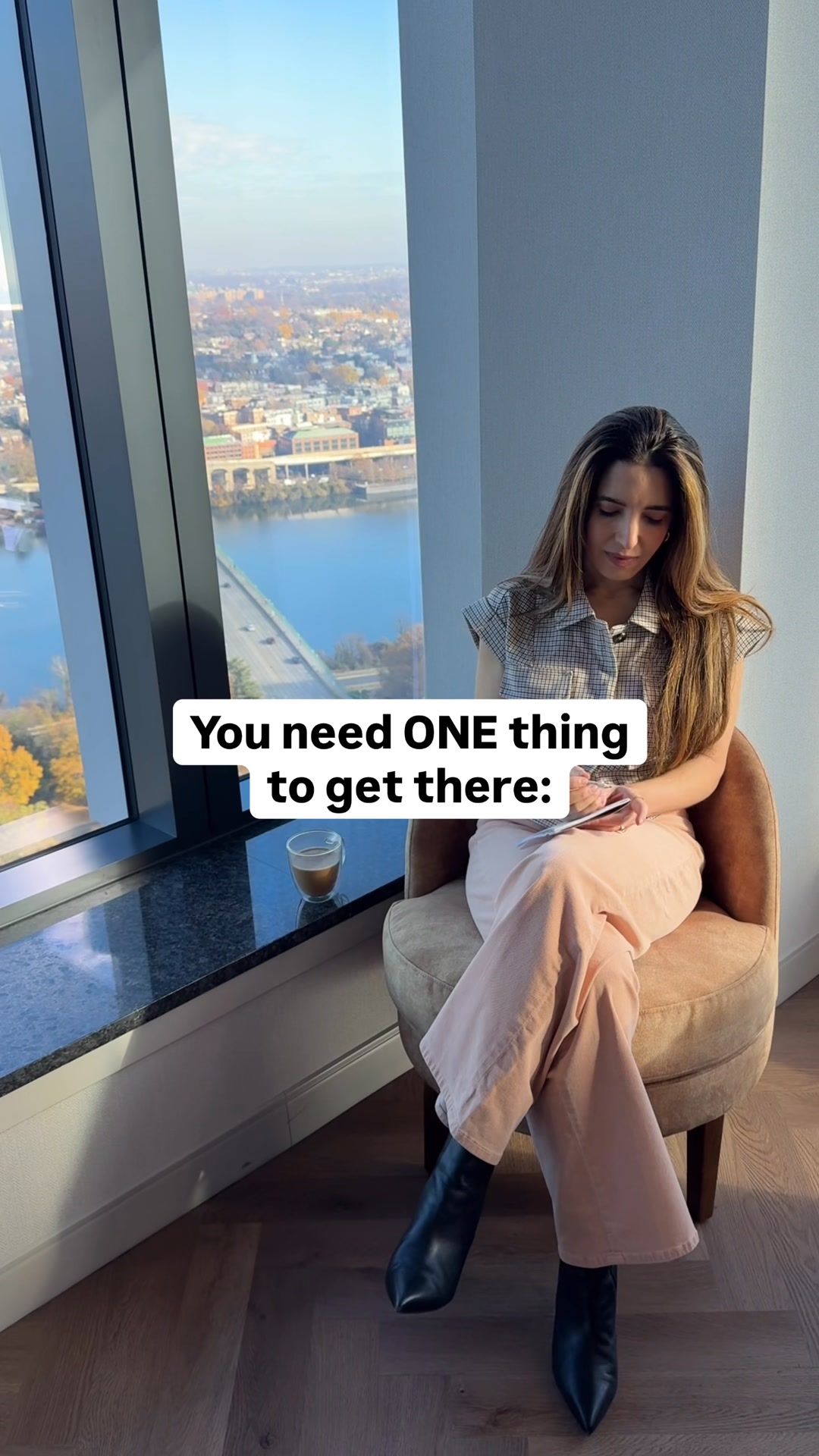 A woman sits in a chair by a large window overlooking a city. She is looking down at a tablet in her hands. White text overlaid on the image reads, "You need ONE thing to get there:". A cup of coffee sits on the windowsill next to her. The overall scene suggests a moment of reflection or planning.