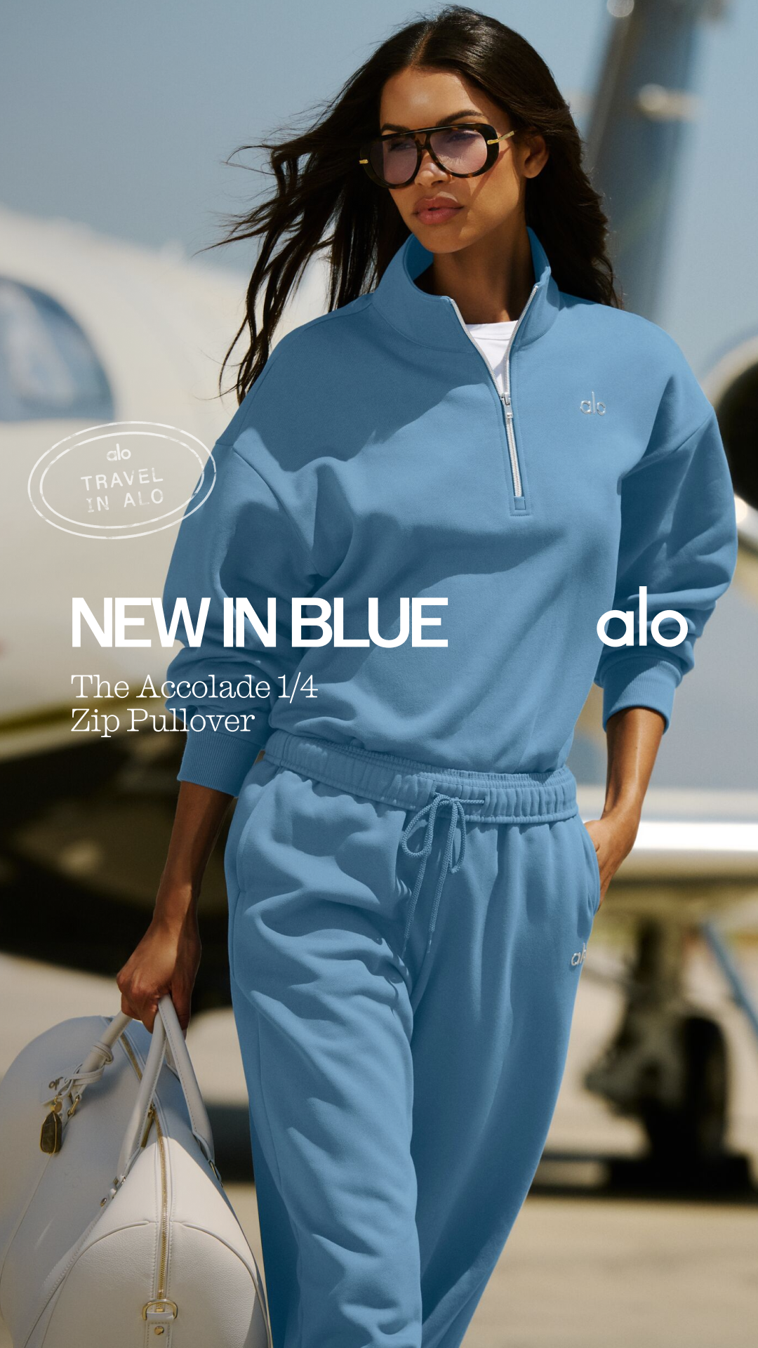 A woman wearing a blue Alo Yoga quarter-zip pullover and matching sweatpants stands in front of a private jet. The text "NEW IN BLUE" is prominently displayed on the left side of the image, with "The Accolade 1/4 Zip Pullover" below it. A circular graphic in the upper left corner reads "ALO TRAVEL IN ALO". The Alo Yoga logo is visible on the pullover and in the upper right corner.