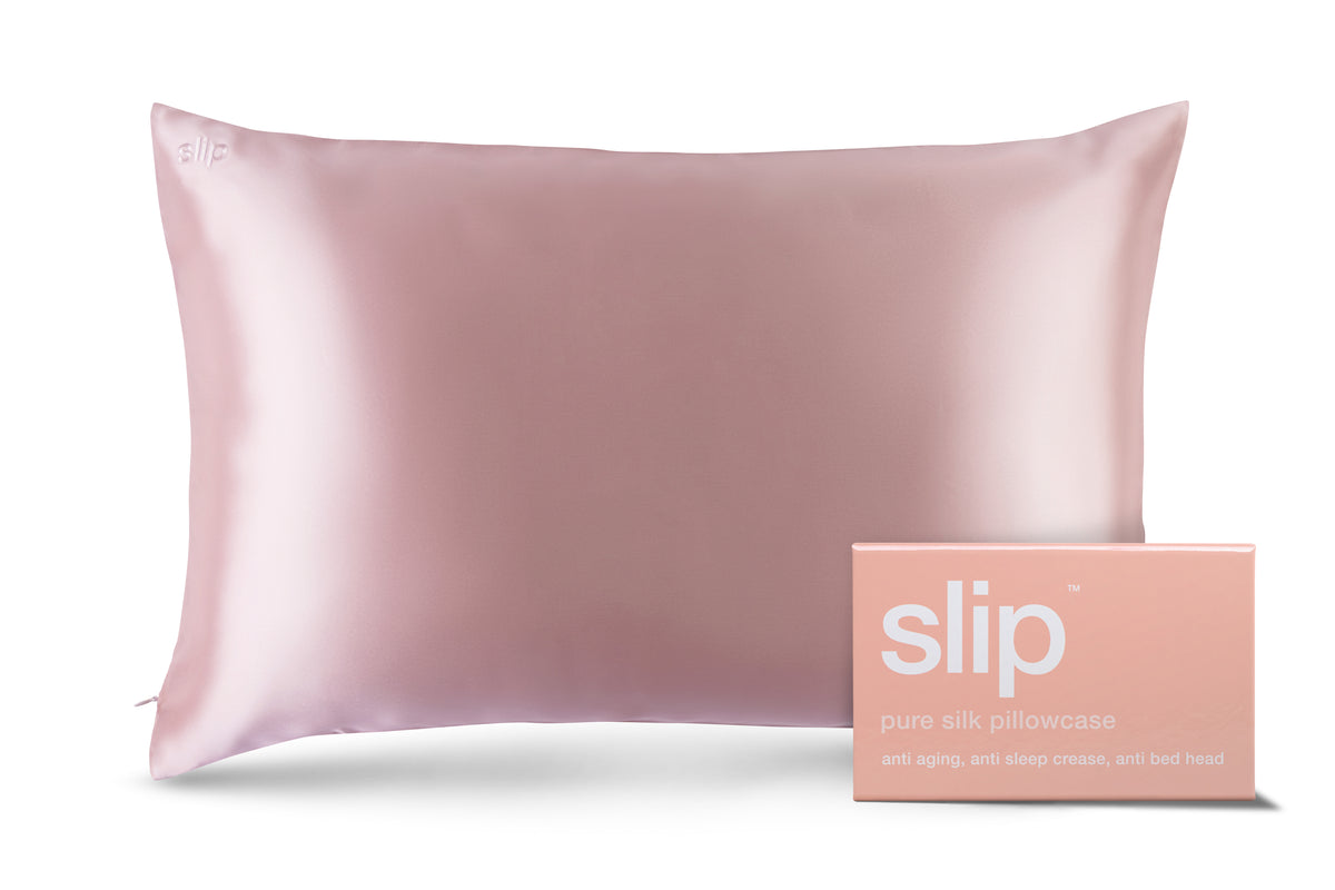 A pink silk pillowcase and its matching box packaging are displayed against a white background. The pillowcase has the brand name 'slip' subtly embroidered in white on the top left corner. The box packaging, positioned to the right of the pillowcase, also features the 'slip' logo in large white lettering. Below the logo, it reads 'pure silk pillowcase' and then 'anti aging, anti sleep crease, anti bed head'. The text '15% OFF YOUR FIRST ORDER' is prominently displayed in white text on a pink banner across the top of the image.