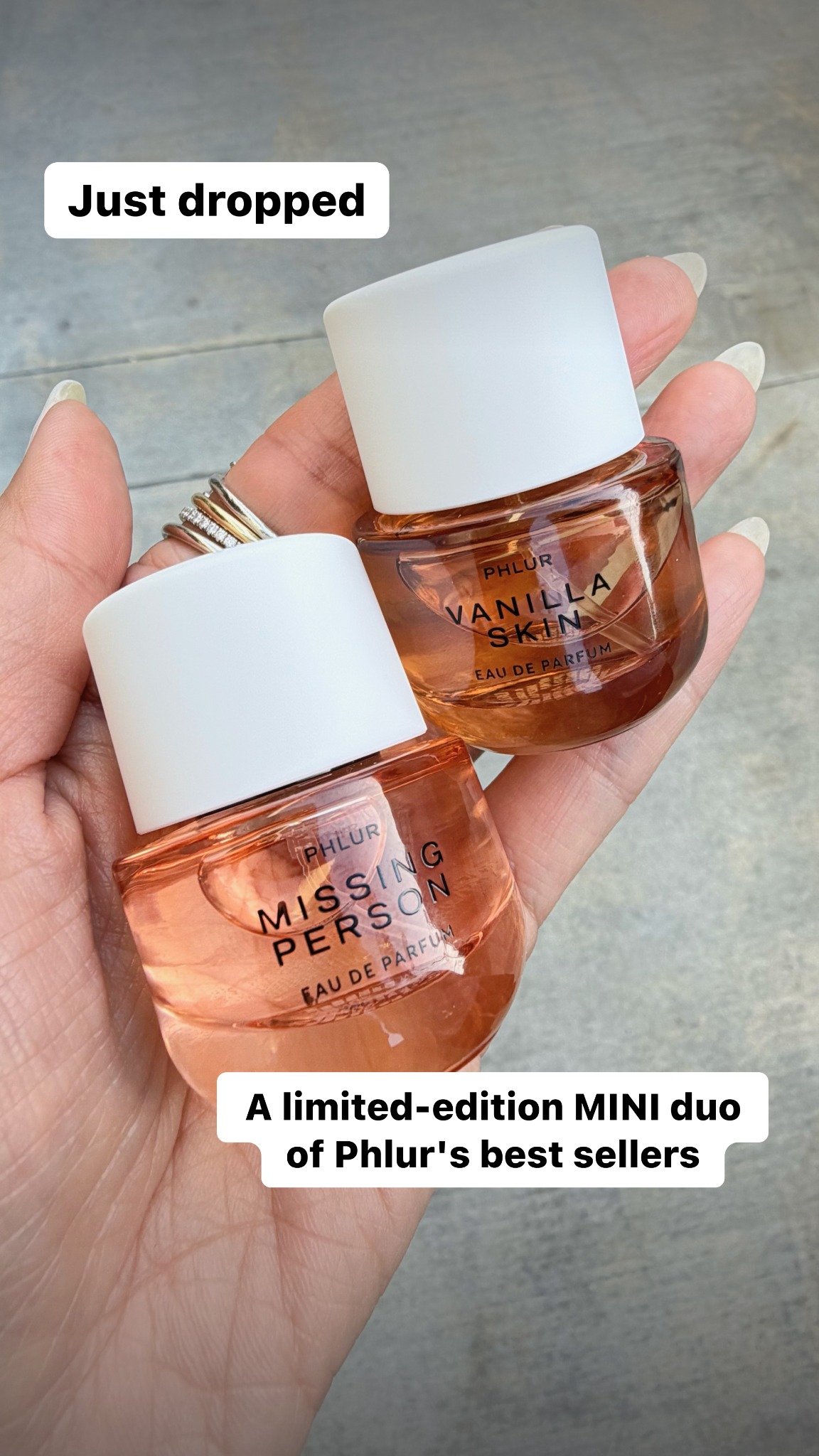 A hand holds two small bottles of Phlur perfume, one labeled "MISSING PERSON" and the other "VANILLA SKIN." The text "Just dropped" appears in a white speech bubble in the upper left corner. Below the bottles, another white speech bubble contains the text "A limited-edition MINI duo of Phlur's best sellers." The perfumes are amber-colored and have white caps.