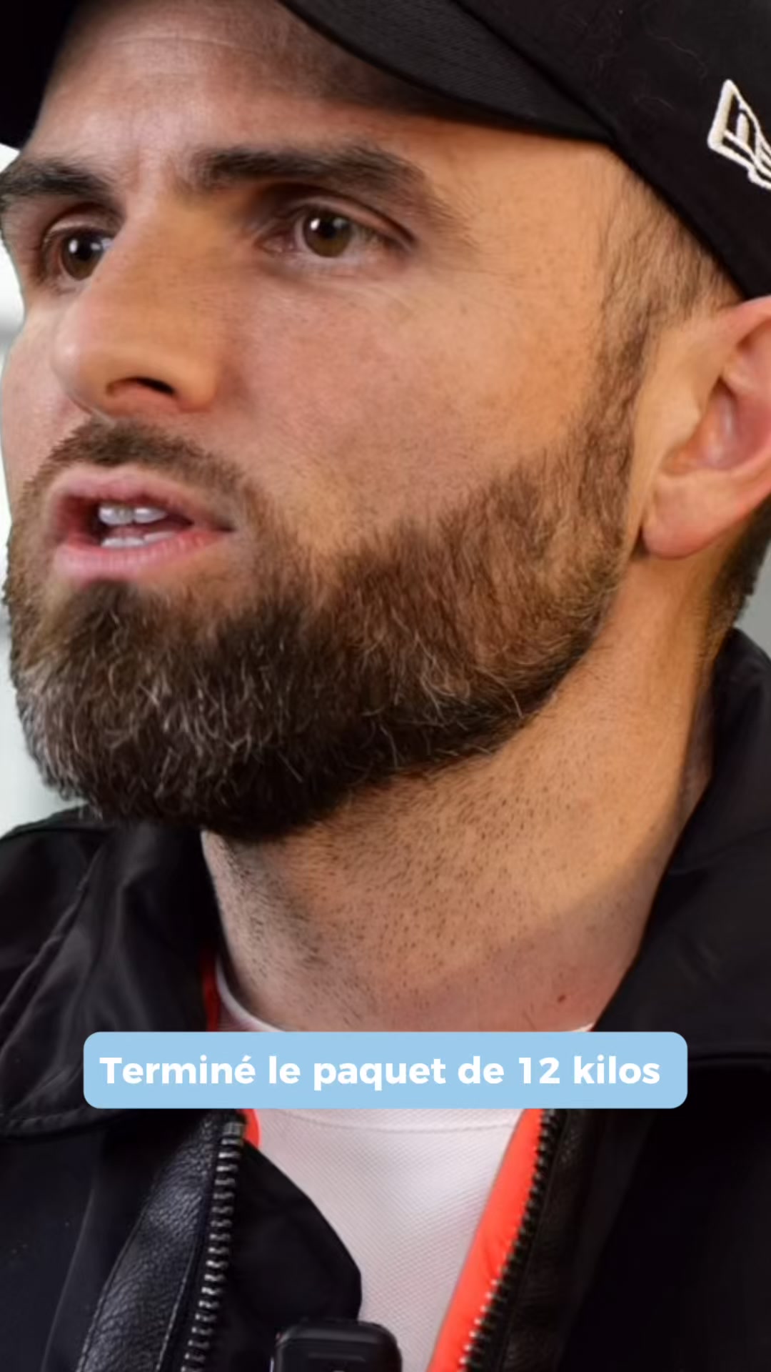 A close-up shot of a man's face and neck, wearing a black baseball cap and a black jacket over a white shirt with orange trim. He has a beard and is looking slightly off-camera with his mouth open. A light blue banner across the bottom of the image contains white text that reads "Terminé le paquet de 12 kilos", which translates to "Finished the 12 kilo package". The creative appears to be a bold claim about weight loss.