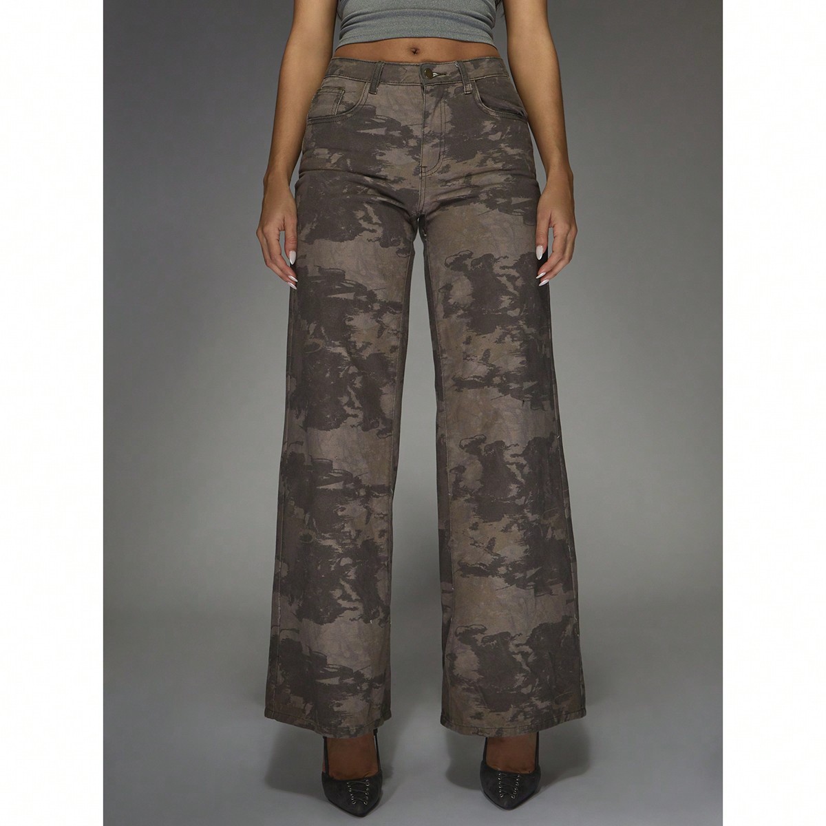 A full-body studio shot of a person wearing camouflage wide-leg pants and a grey crop top. The text "Effortless, but make it iconic" is overlaid on the image. The background is a plain grey gradient. The model is wearing black pointed-toe heels.