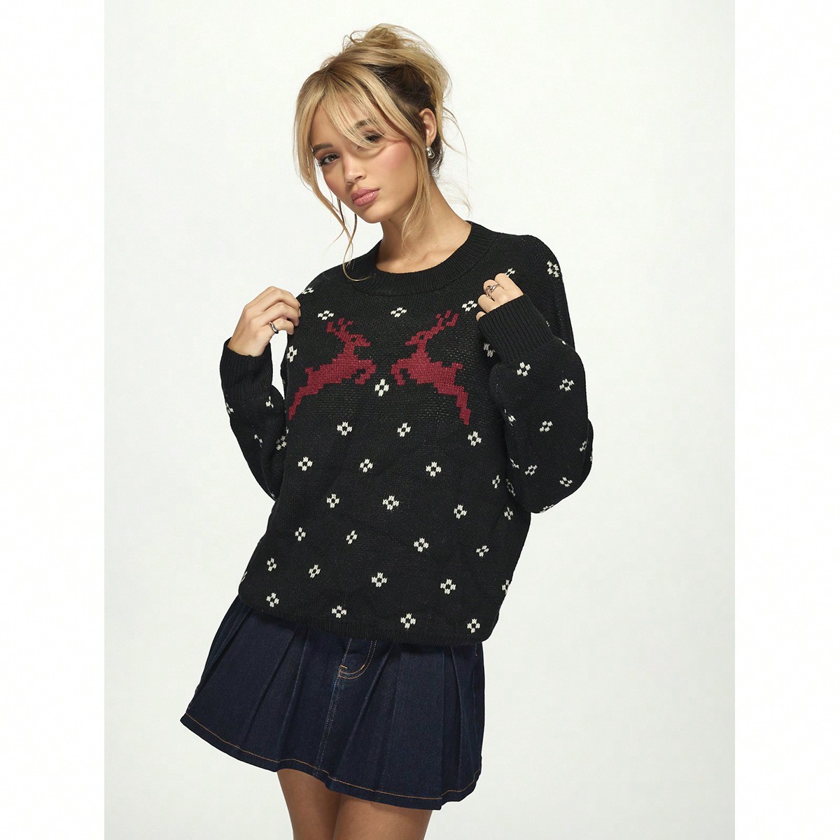 A young woman with blonde hair styled in a messy bun and bangs poses against a white background. She is wearing a black crewneck sweater with a red reindeer pattern and a dark denim mini skirt. The text "New season. same you. better outfits." is overlaid on the image. She is looking at the camera with her hands on the sweater.