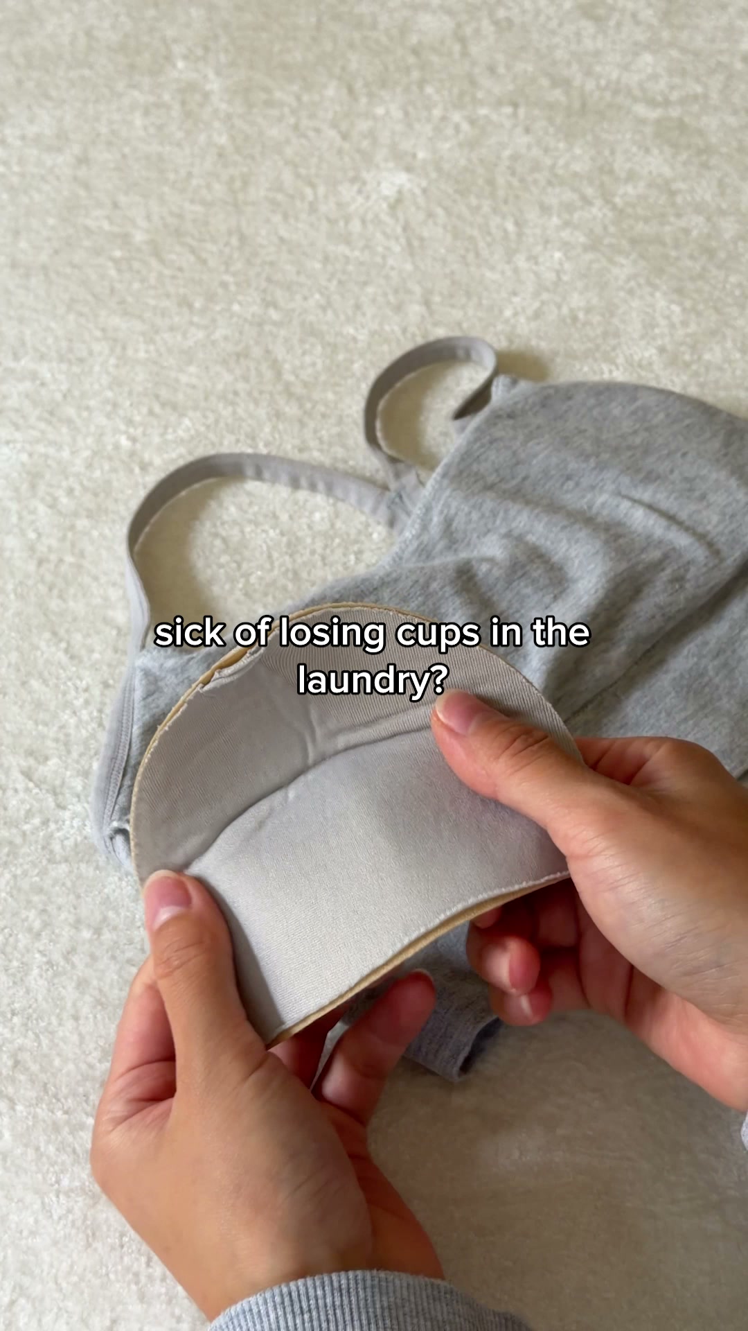 A close-up shot shows a person holding the inside of a grey bralette. The text "sick of losing cups in the laundry?" is overlaid on the image. The bralette appears to have built-in cups that are being demonstrated.