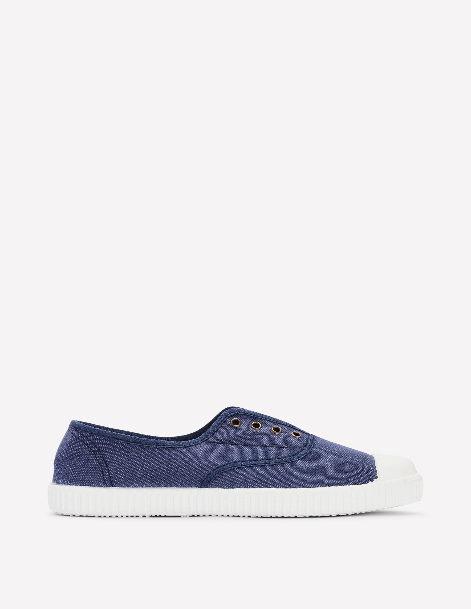A studio shot of a single blue canvas sneaker with a white toe cap and white sole. The shoe is shown from the side, facing left, with no laces. The background is a plain, light grey. The text "Craquez maintenant, portez longtemps : découvrez des modèles bien conçus, inspirés du patrimoine britannique avec une touche d’espièglerie." is overlaid on the image.