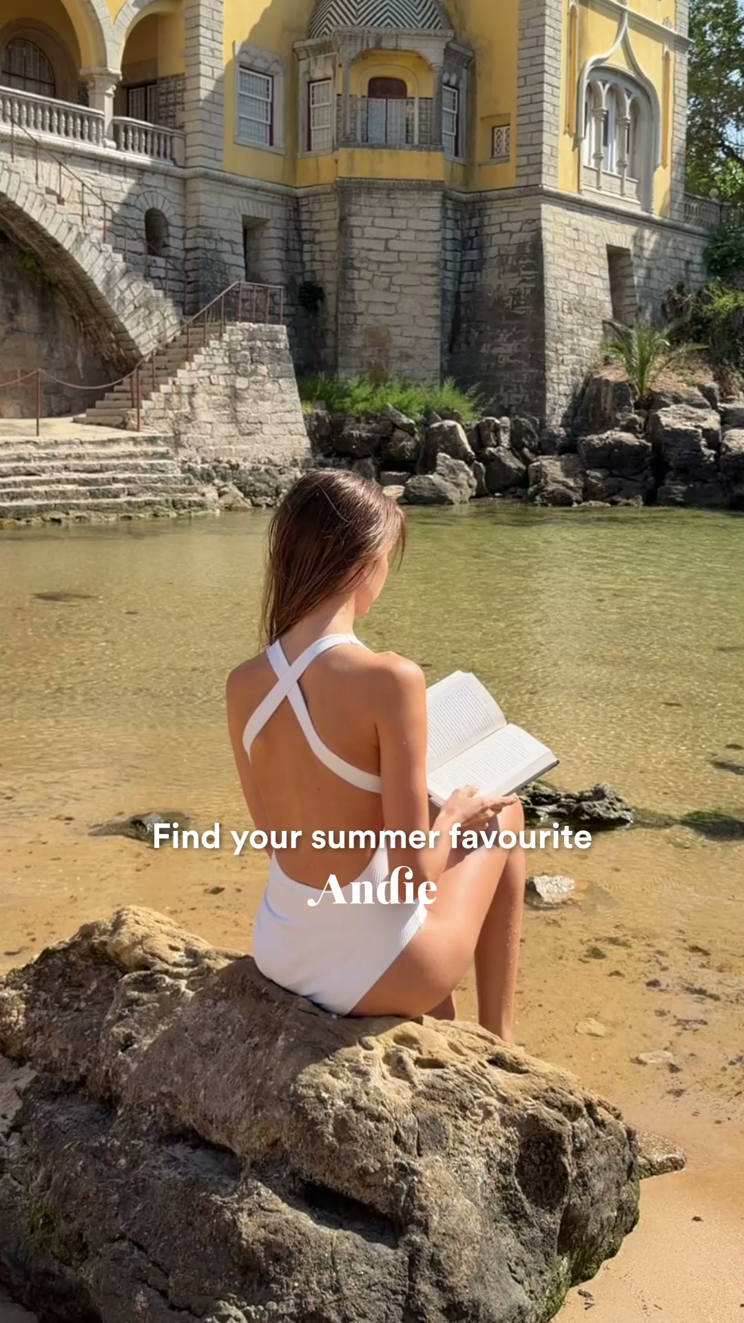 A young woman in a white swimsuit sits on a rock by the water, reading a book. The background shows a large, ornate yellow building with stone stairs leading down to the water. White text overlaid on the image reads "Find your summer favourite Andie." The scene evokes a sense of relaxation and enjoyment of summer activities.