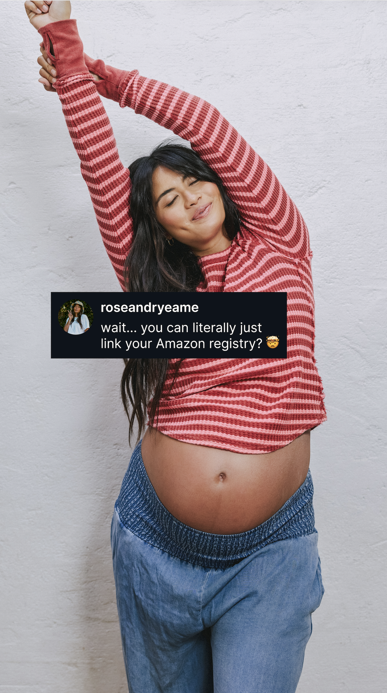 A pregnant woman with her arms stretched above her head is shown against a white brick wall. She is wearing a red and pink striped long-sleeved shirt and blue denim-like pants. A black speech bubble with a profile picture and text is overlaid on the image. The text reads: "roseandryeame wait... you can literally just link your Amazon registry?" with a confused emoji.