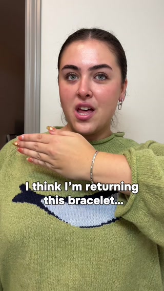 A woman with dark hair and bold eyebrows is wearing a green sweater with a whale design. She is looking at the camera with a slightly concerned expression and her hand is held up in front of her face. White text overlaid on the bottom of the image reads "I think I'm returning this bracelet...". The creative appears to be a personal video from a creator discussing a product.